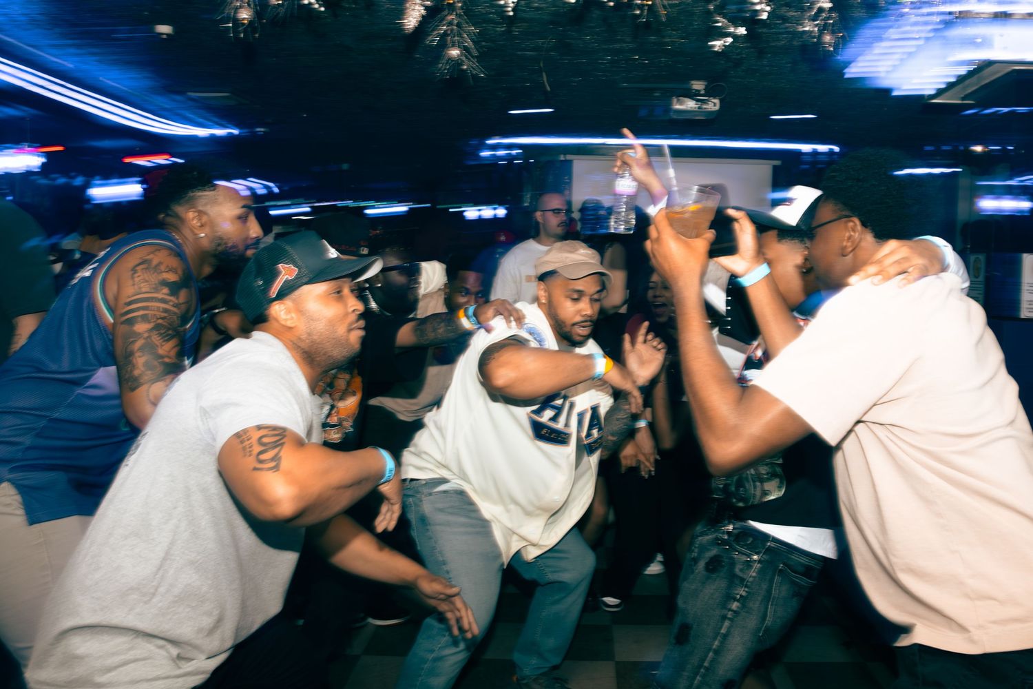 Group of men dancing energetically on a nightclub dance floor under blue lights.