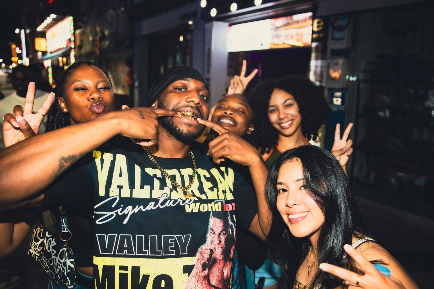 Group of five friends posing with peace signs outside at a fun nighttime event.