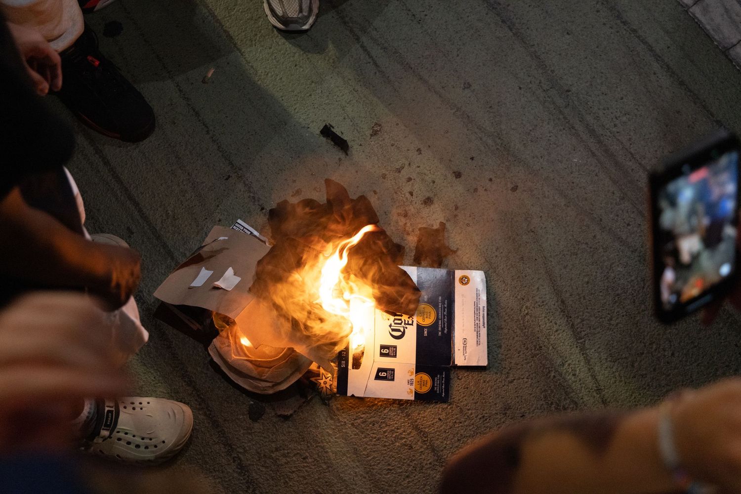 Crowd gathered around burning papers and objects on ground at night protest event.