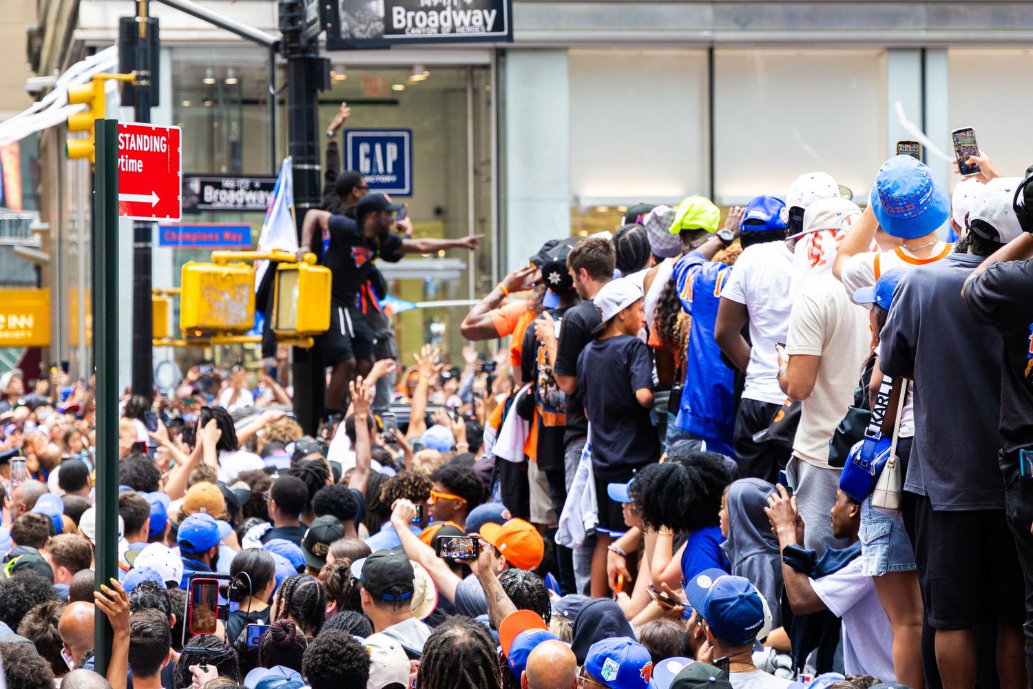 Large crowd gathered on Broadway street in New York City for an outdoor event, with people climbing structures near a GAP store.