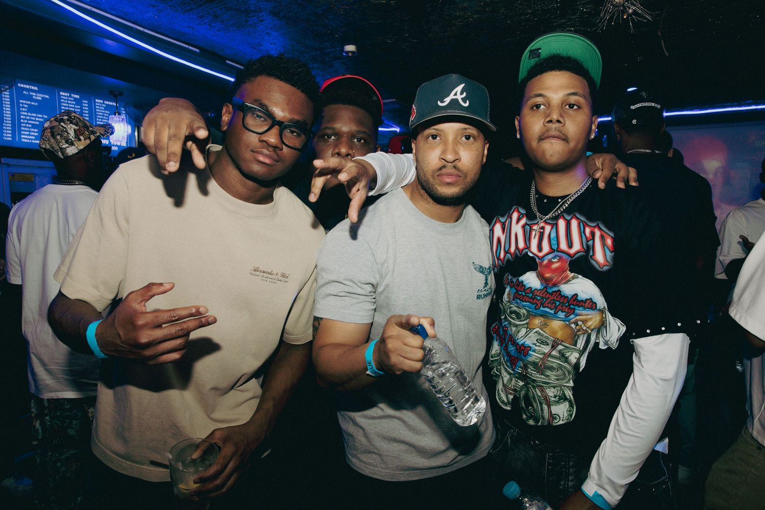 Four young men pose together smiling at a nightclub party under blue lights.