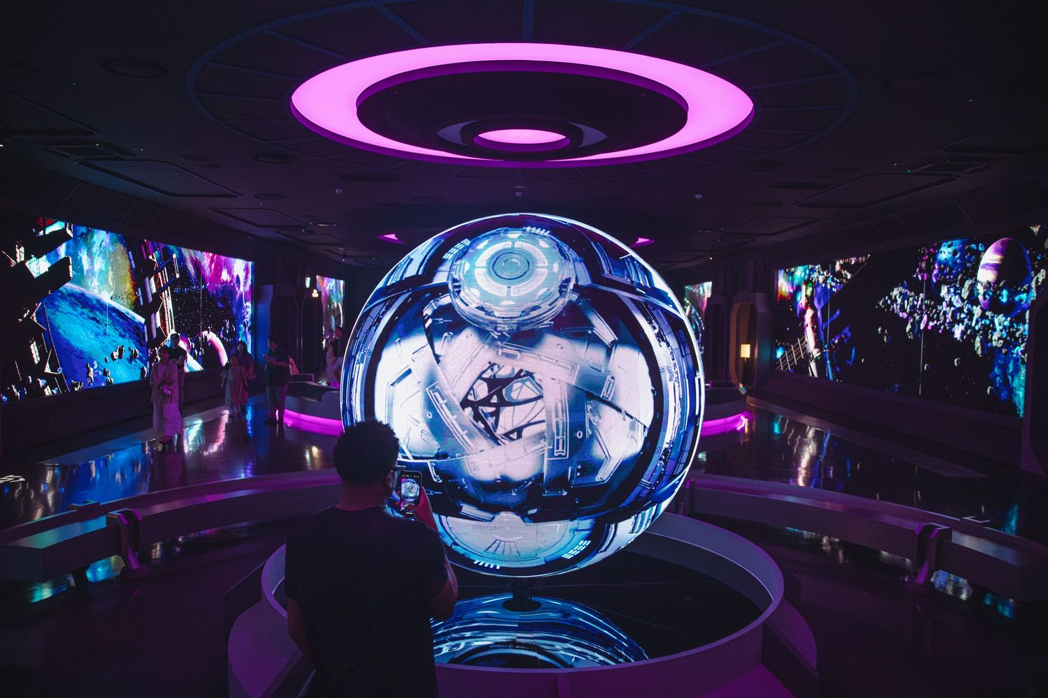 A large reflective sphere displays futuristic imagery surrounded by vibrant LED screens in a high-tech exhibit space.