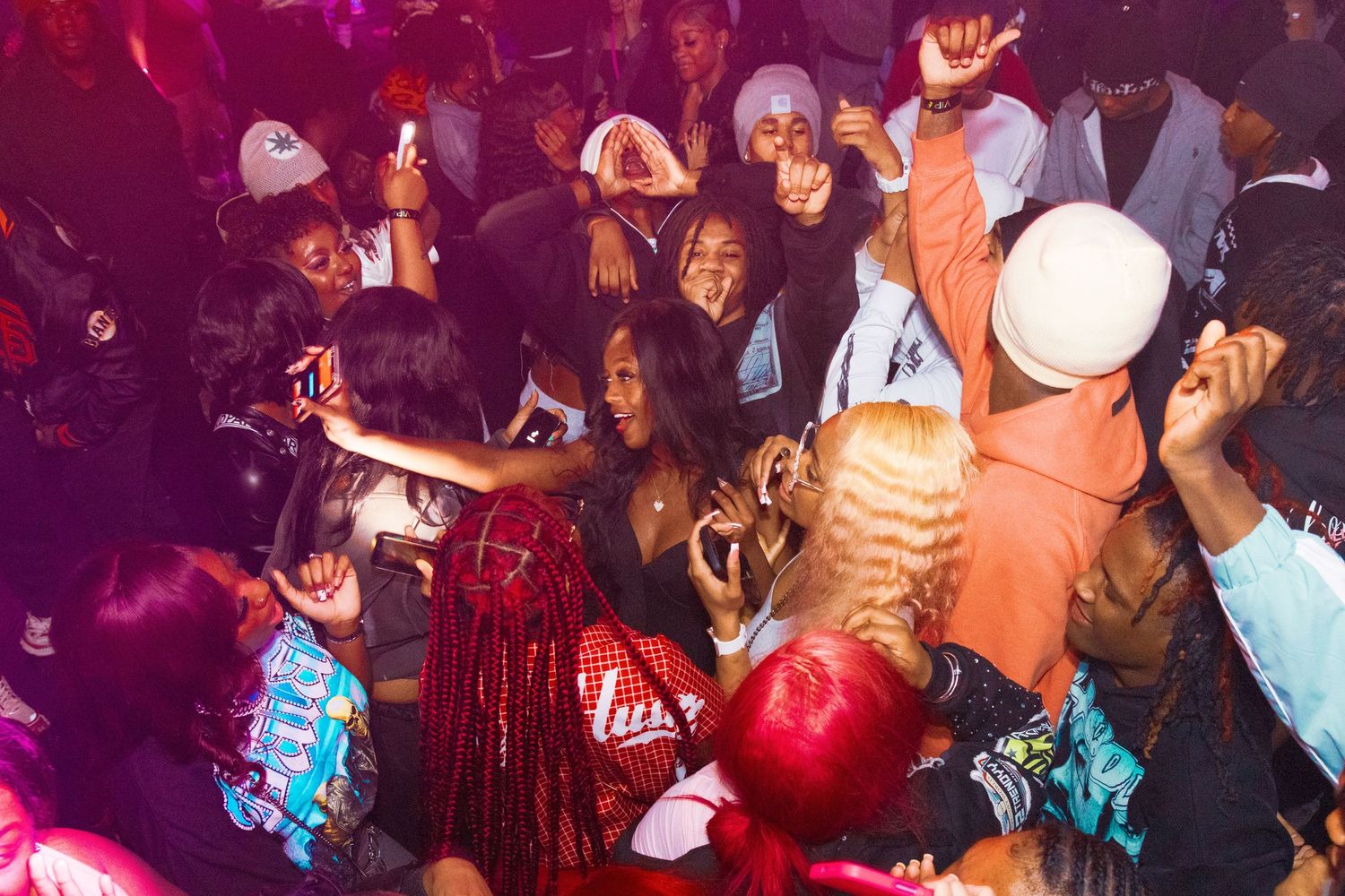 Energetic nightclub crowd dancing and taking selfies at a lively party event with colorful lighting.