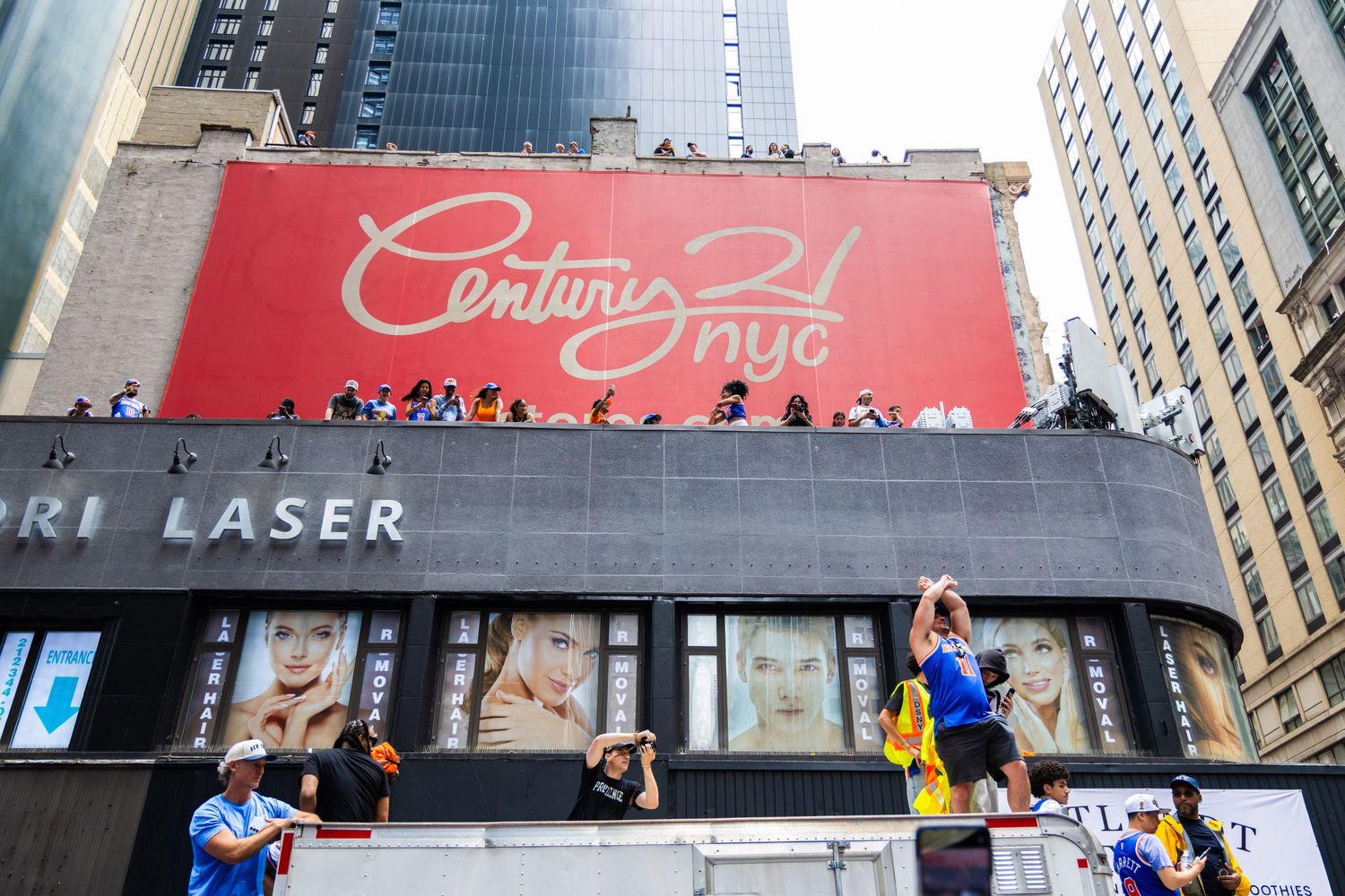 Crowd gathers on a rooftop below a Century 21 NYC red billboard in bustling New York City.