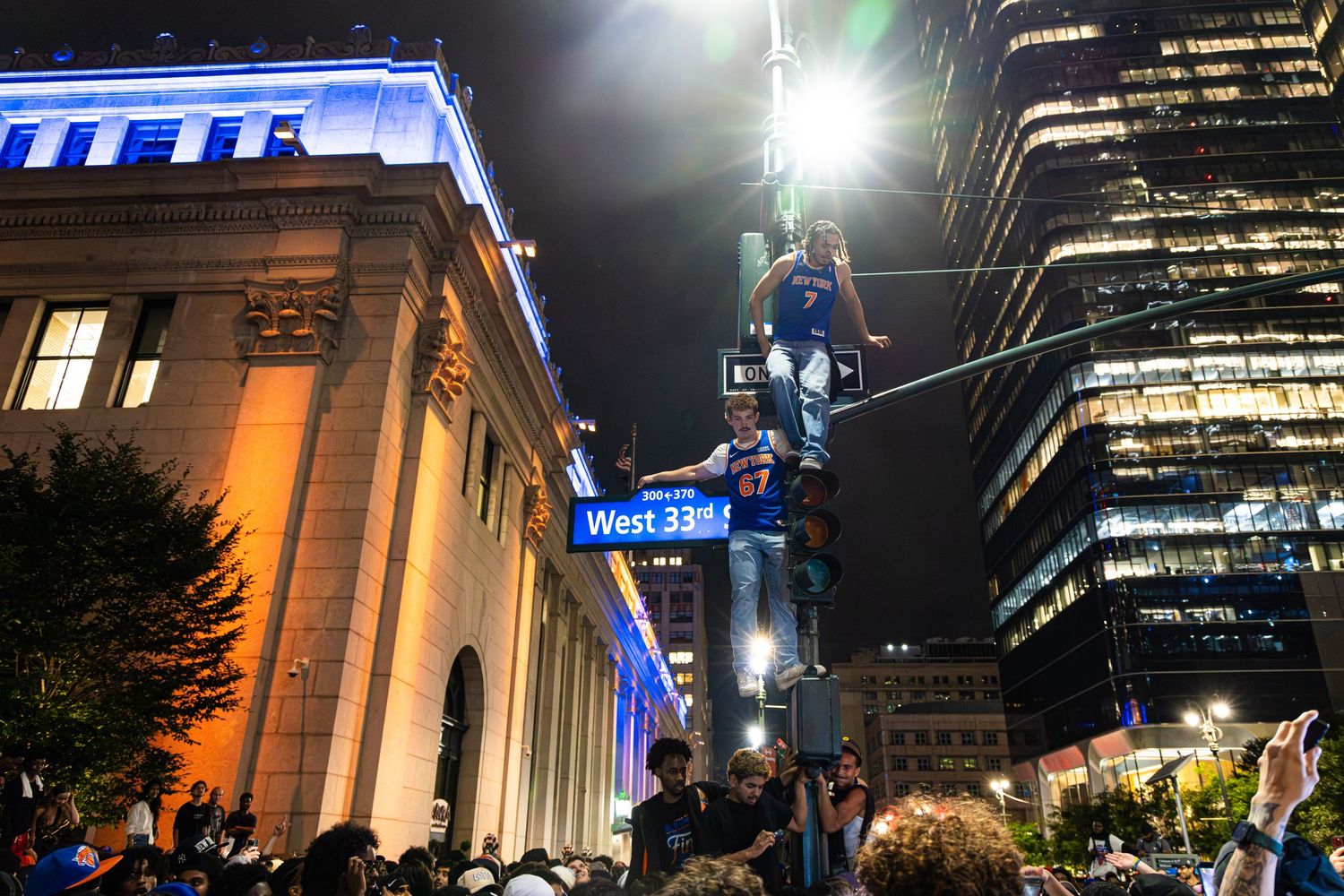 Crowd celebrating at night near West 33rd Street sign in New York City with illuminated skyscrapers.