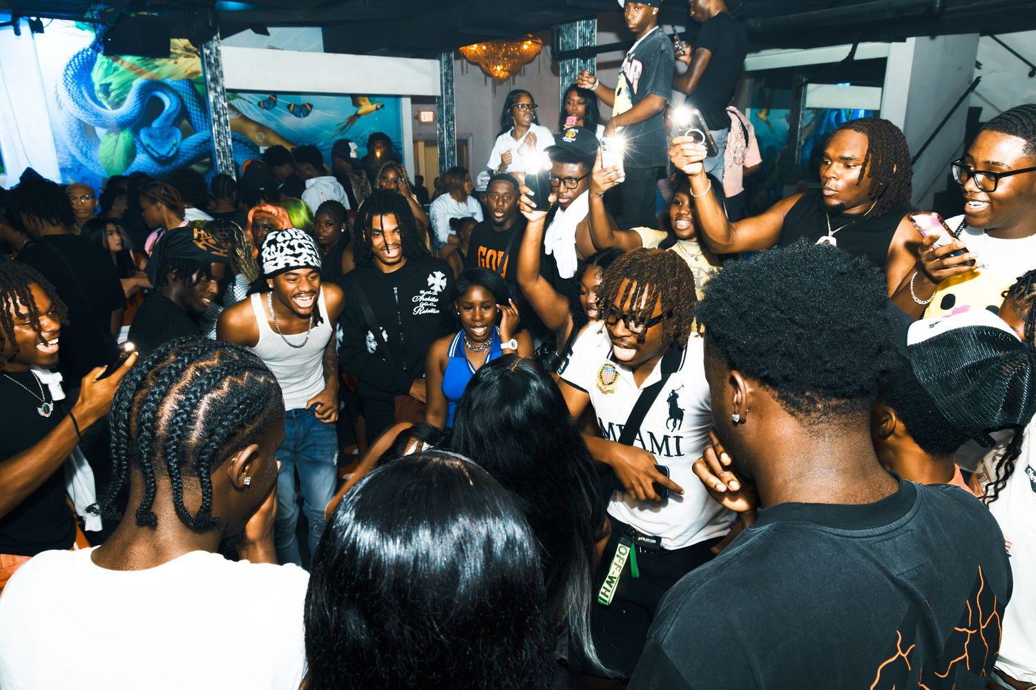 Energetic indoor party scene with a diverse crowd of young people dancing and celebrating together.
