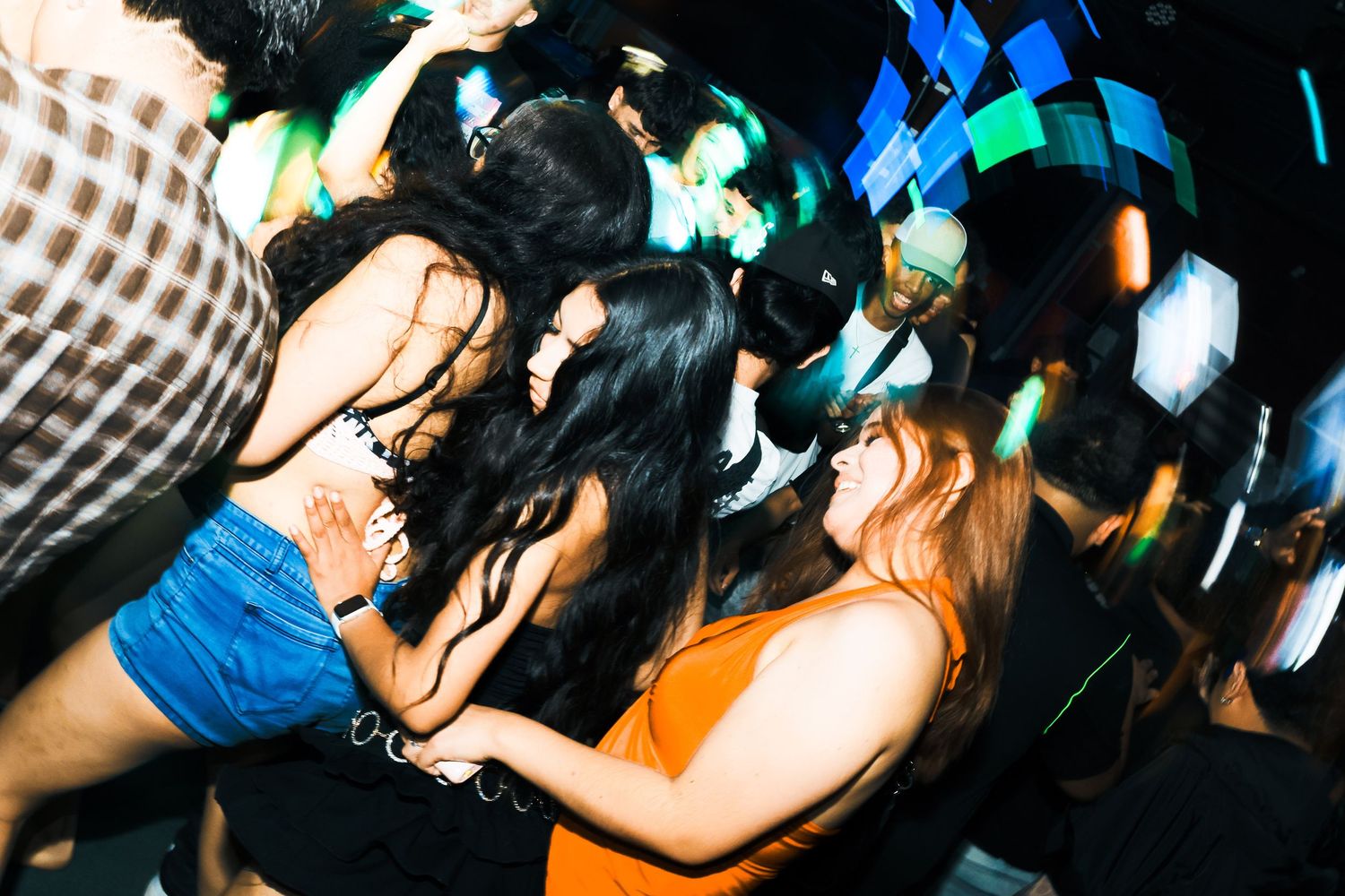 People dancing energetically at a nightclub with colorful lights and a lively atmosphere.