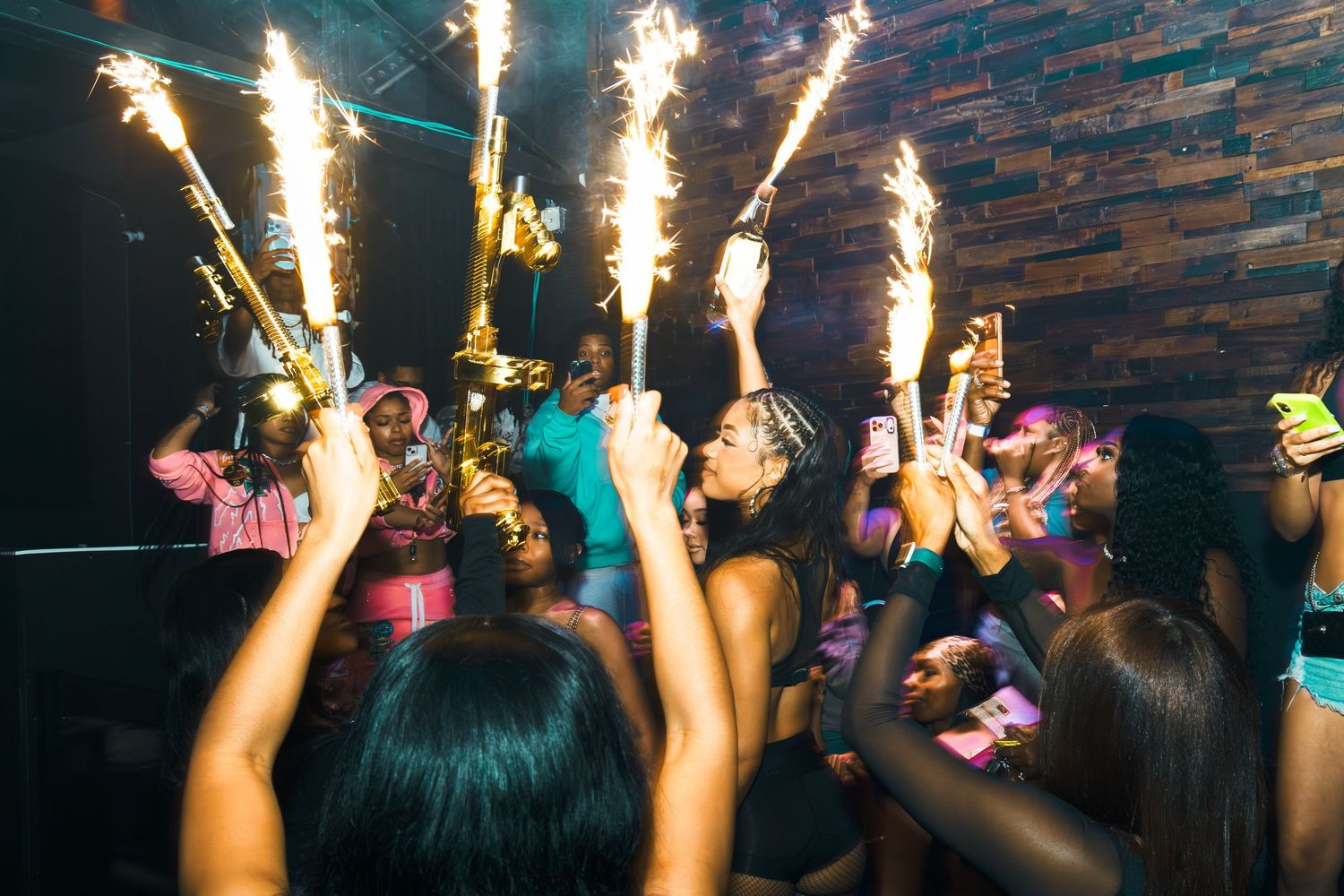 Group of women celebrating at a nightclub party with sparklers and champagne in a dark venue.