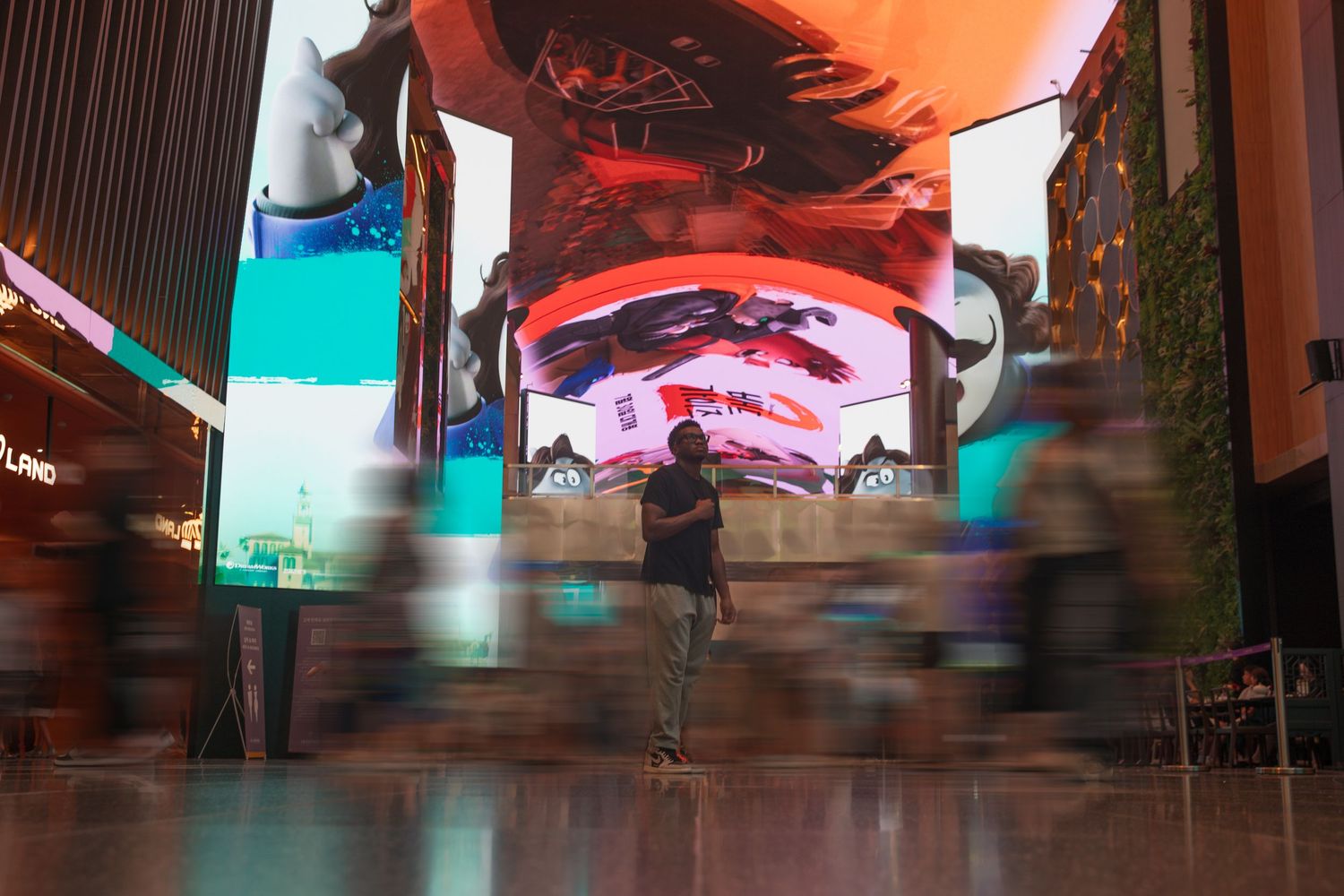 People walk through a vibrant mall atrium with large colorful LED display screens illuminating the modern interior.