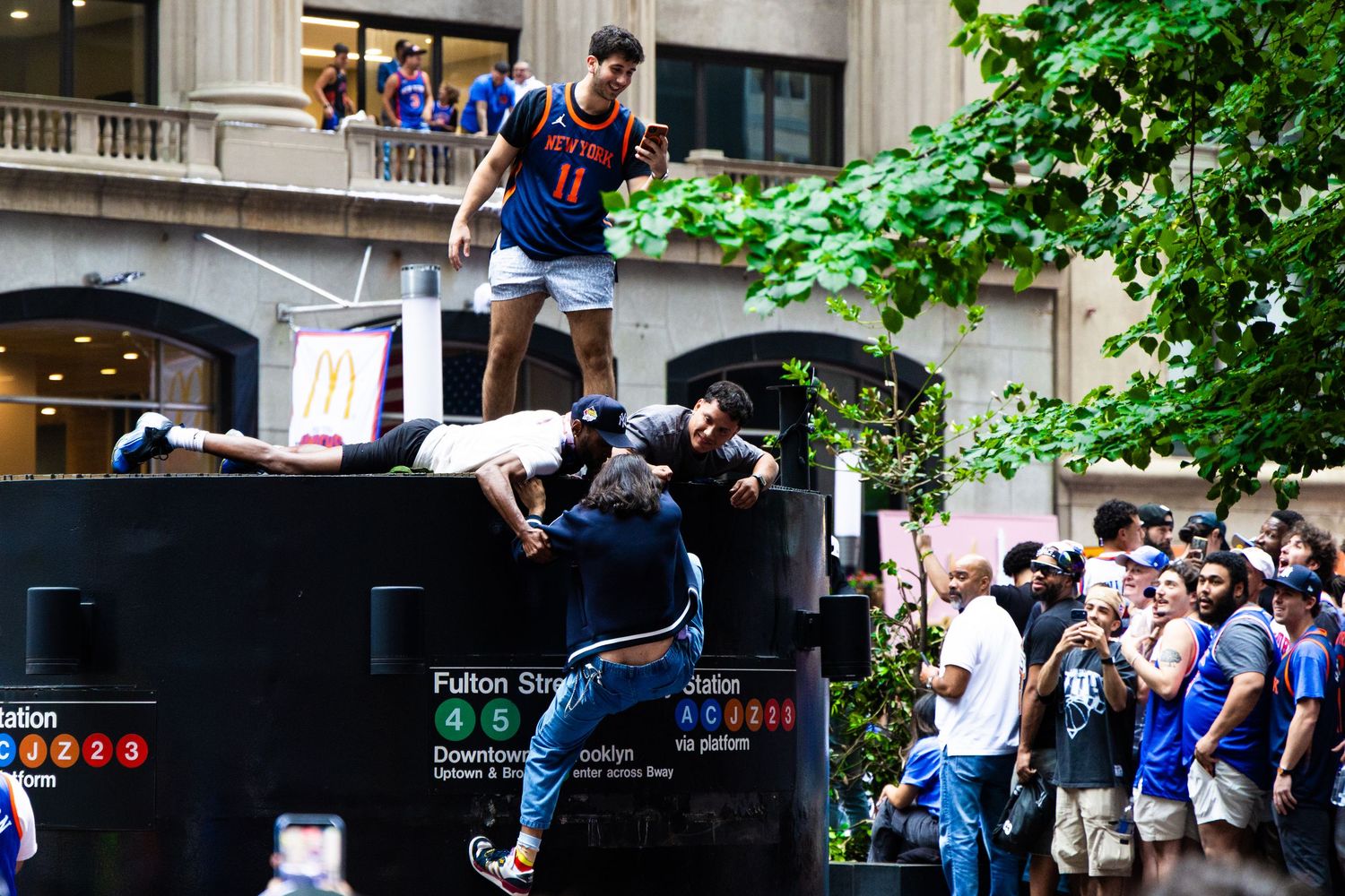 Fans celebrate atop Fulton Station subway entrance during a street parade in New York City.