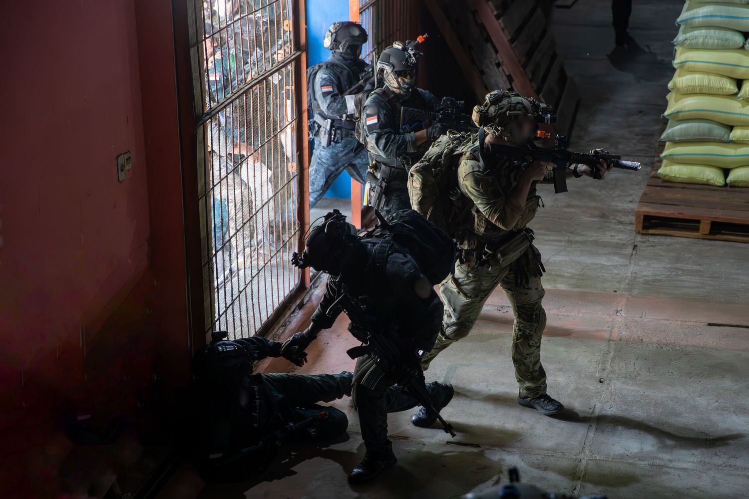 Armed tactical military unit breaching a building entrance during special operations training exercise.