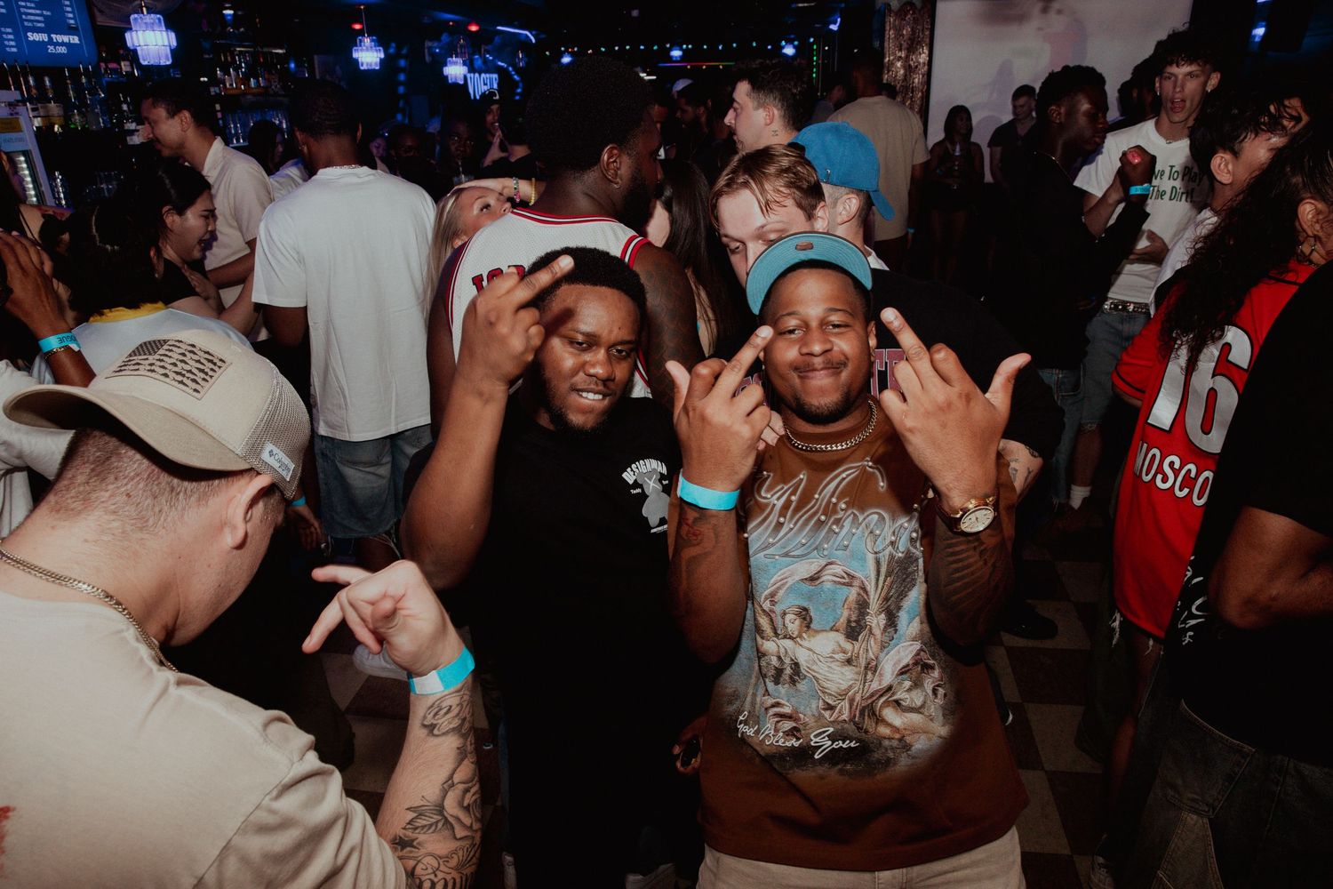 Two men making hand gestures and smiling at a lively nightclub party event.