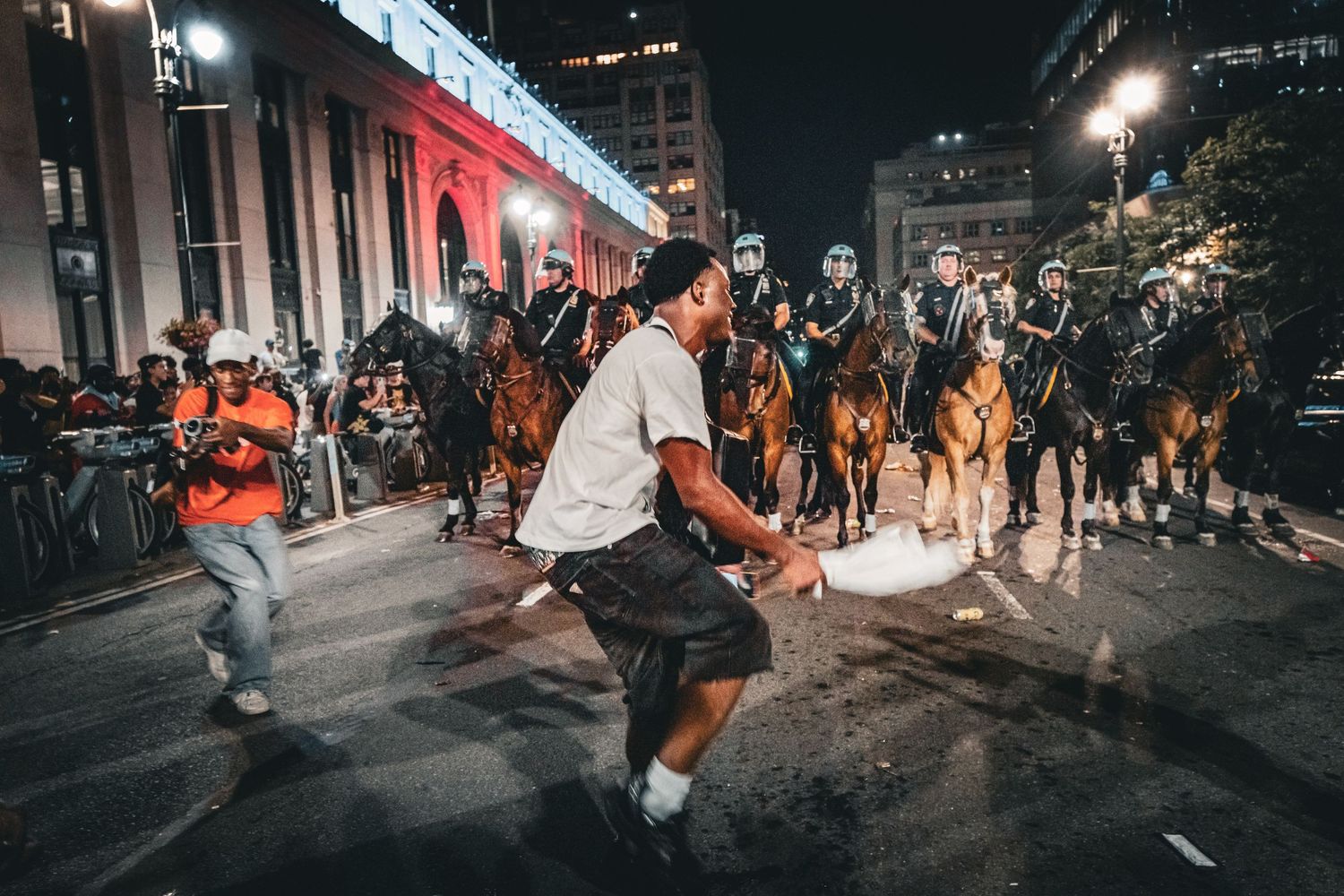 Mounted police officers line up on a city street at night facing pedestrians during a protest.