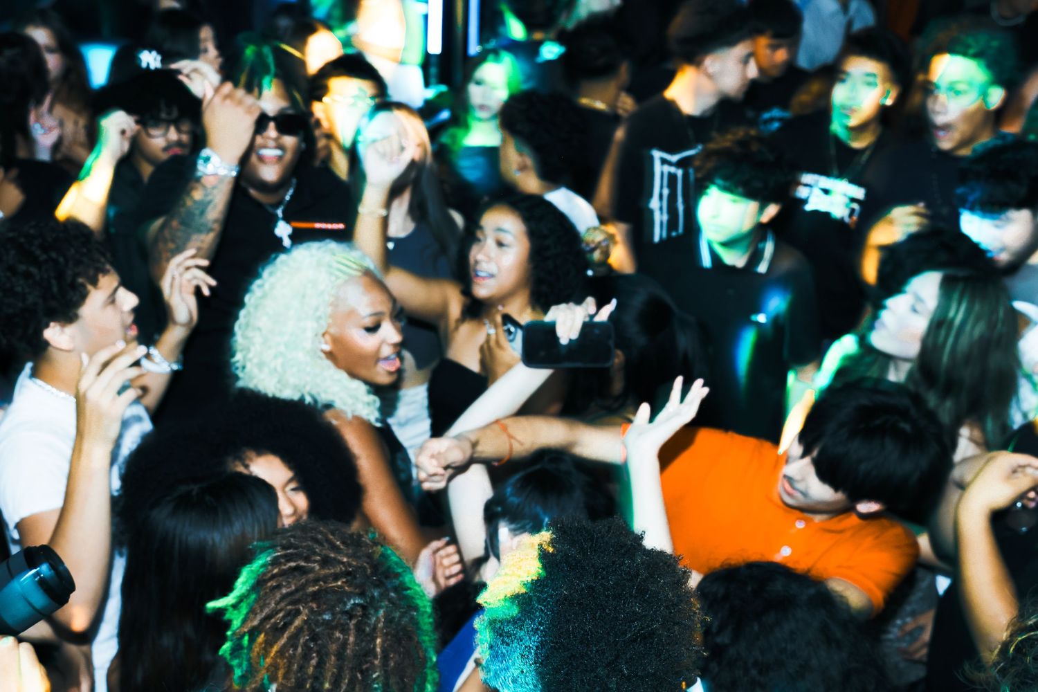 Energetic crowd at a nightclub party with a blonde performer engaging fans under green lights.