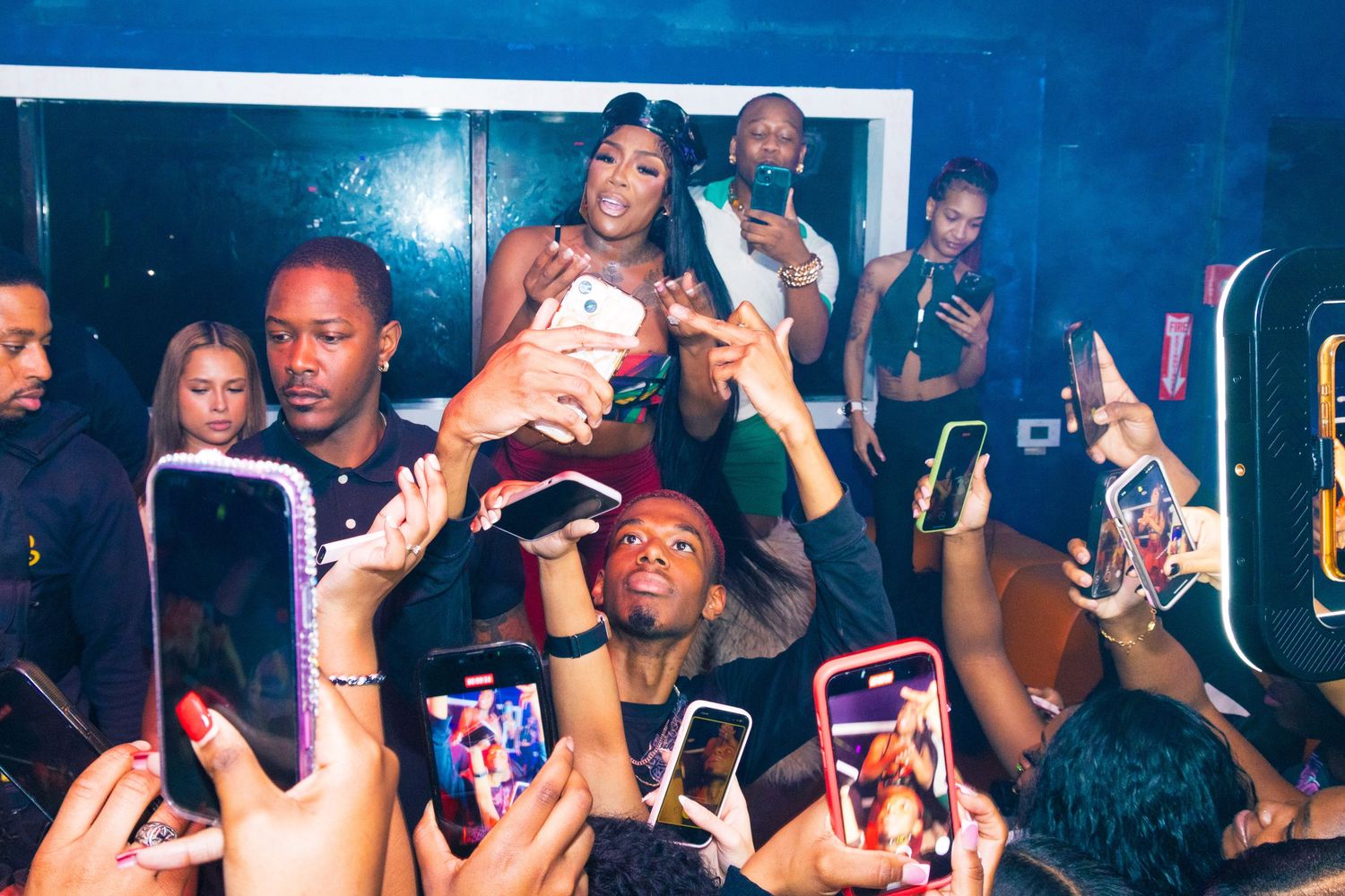 Crowd at a nightclub event with fans holding phones to photograph a performer on stage.