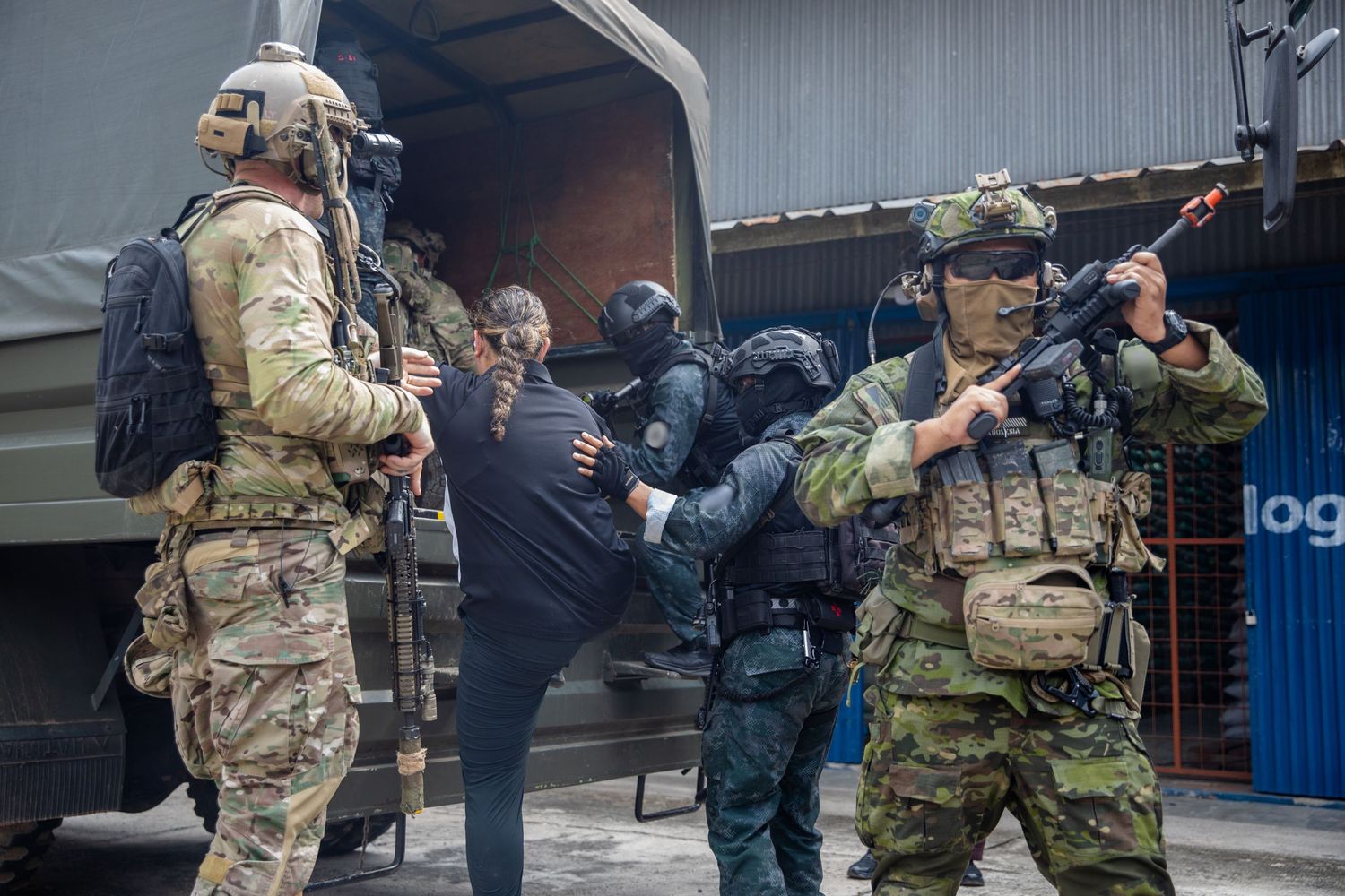 Armed tactical soldiers detain a suspect near a military truck during a law enforcement operation.