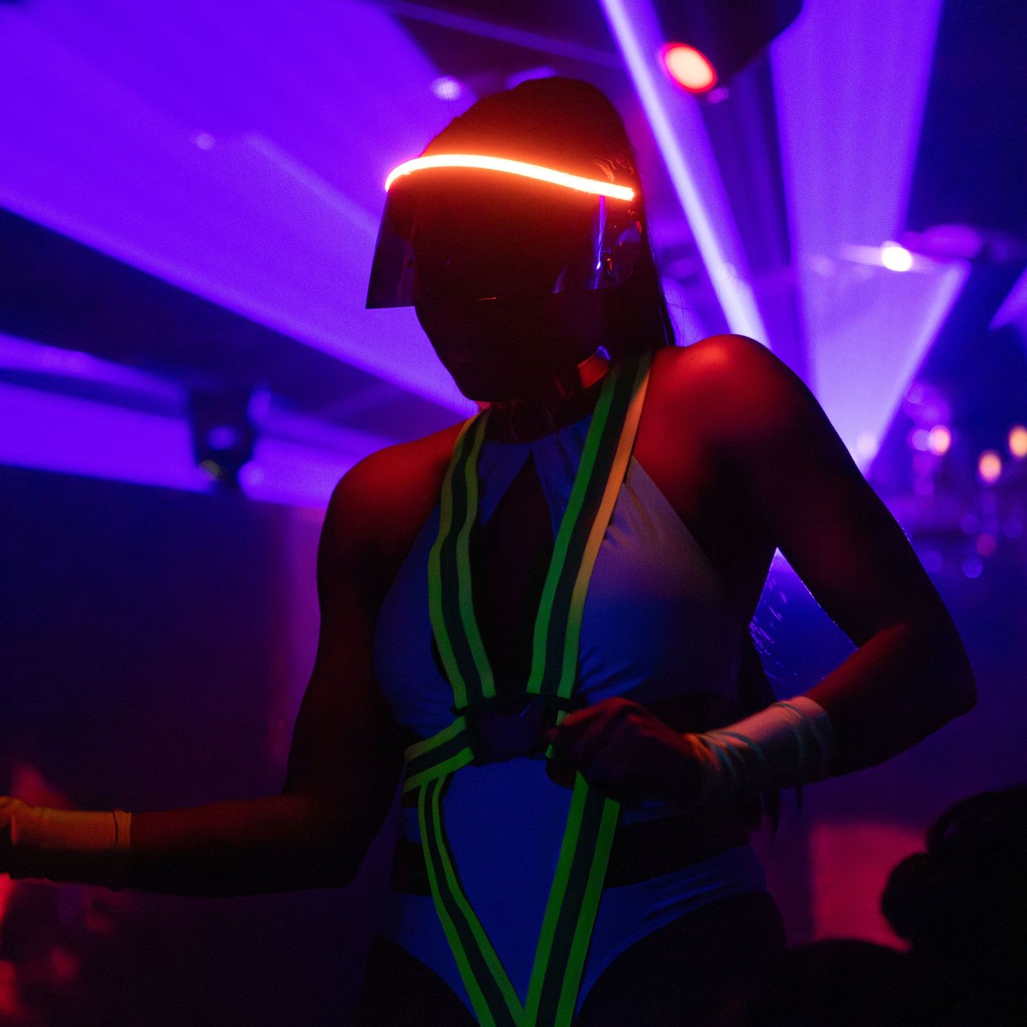 Performer in neon glowing costume and lit visor helmet dancing at a UV nightclub party event.