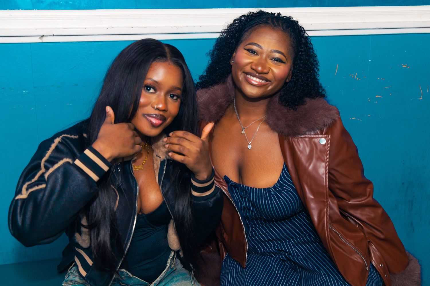 Two smiling women posing together against a blue wall, wearing stylish outfits at a social event.