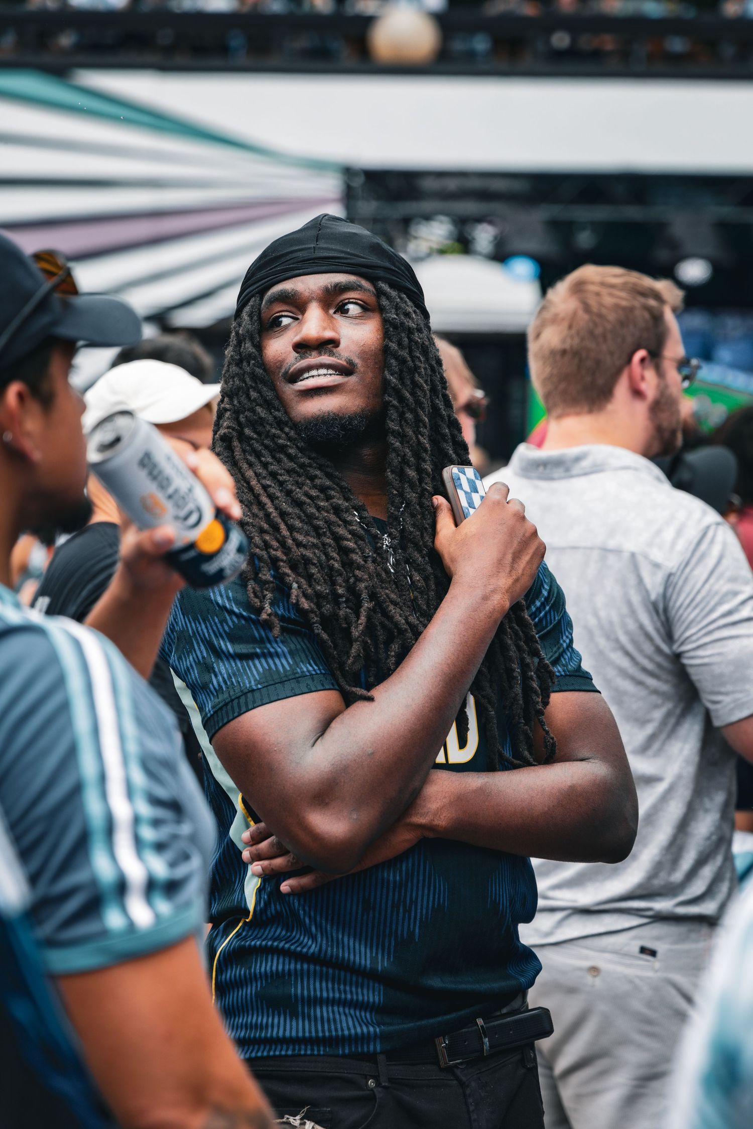 A young Black man with long dreadlocks and a dark bandana enjoys an outdoor music festival crowd.