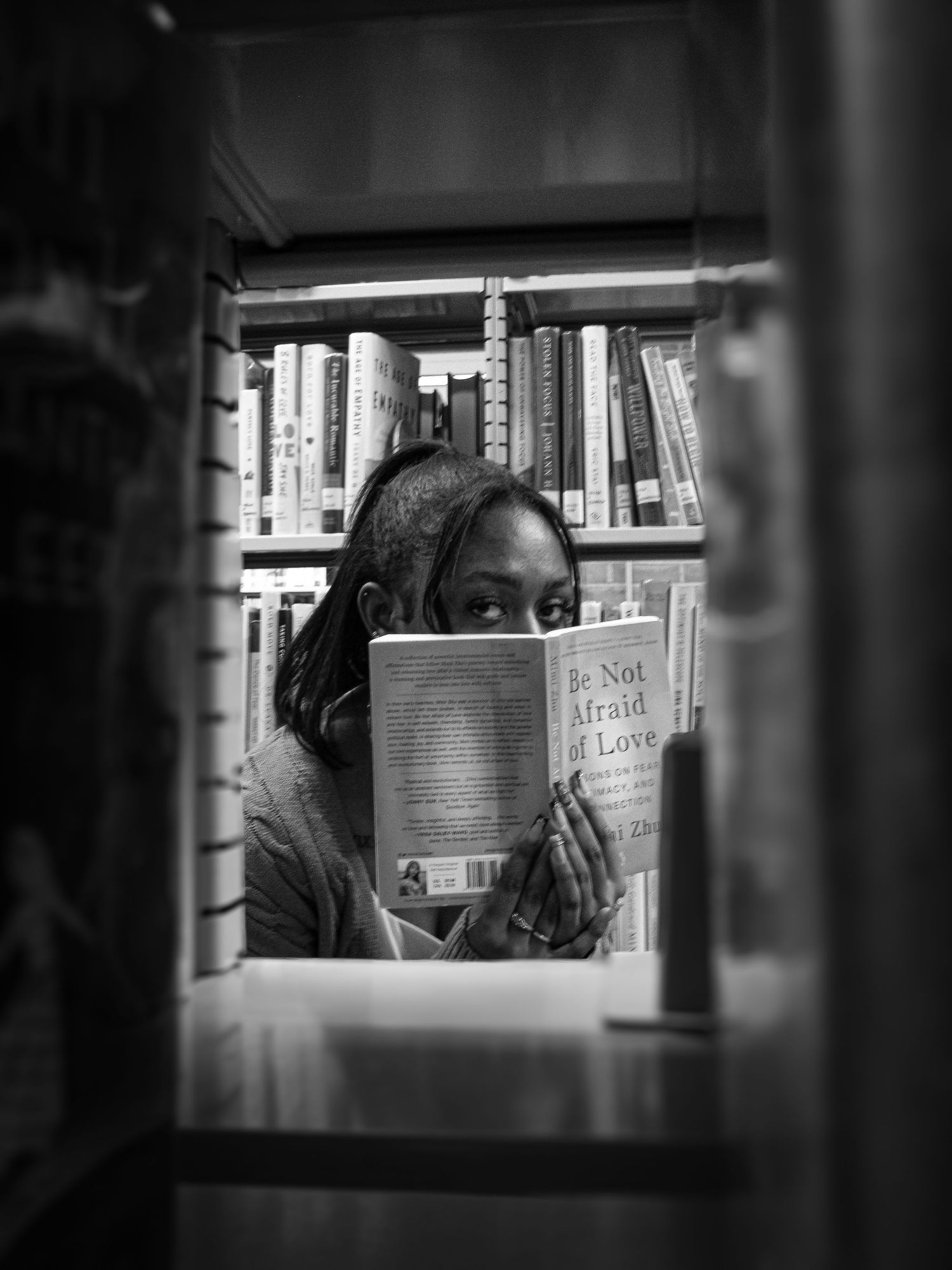 Person reading a book between library shelves in dramatic black and white lighting.