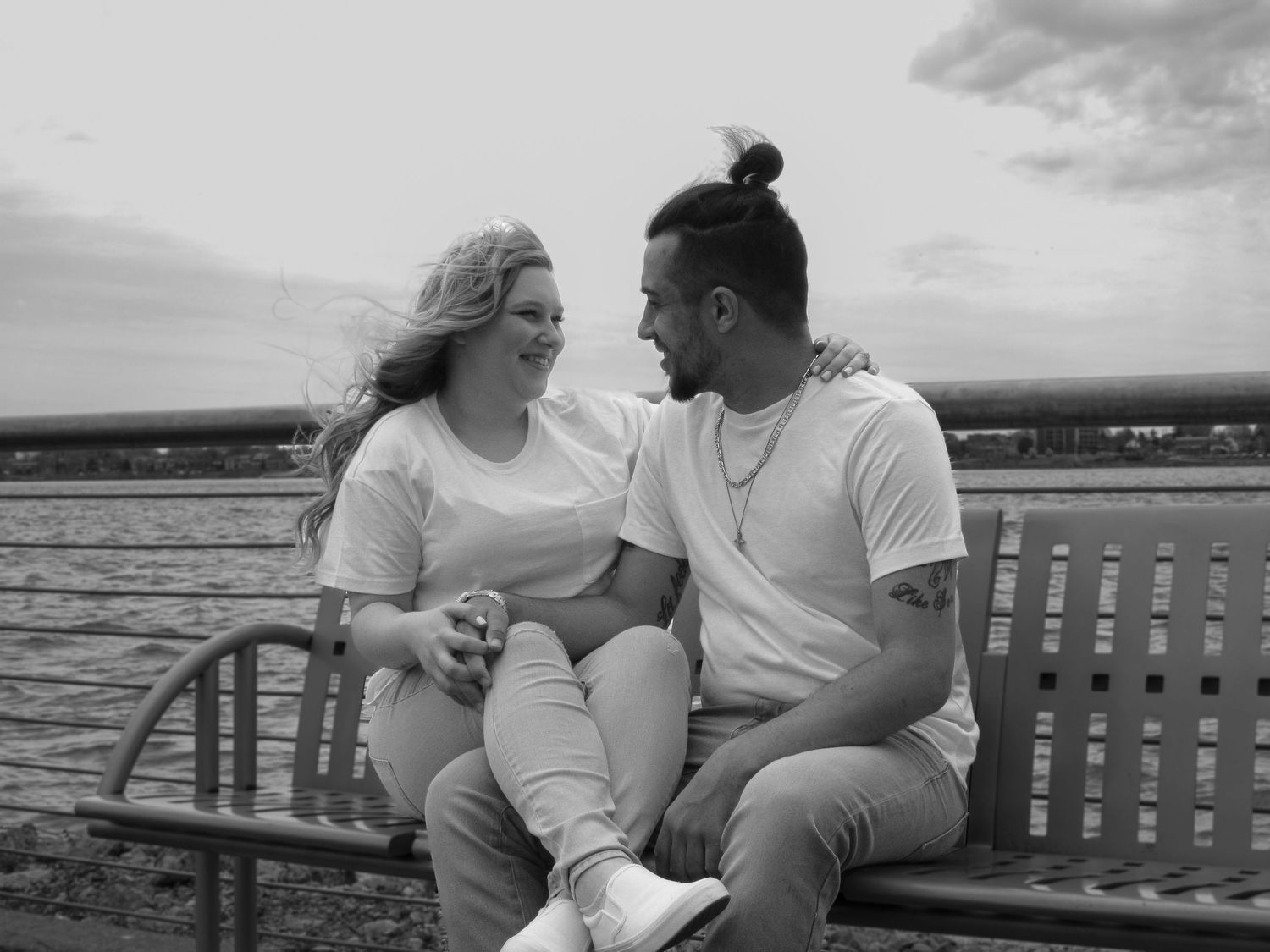 Romantic moments captured in black and white along a waterfront bench at sunset.