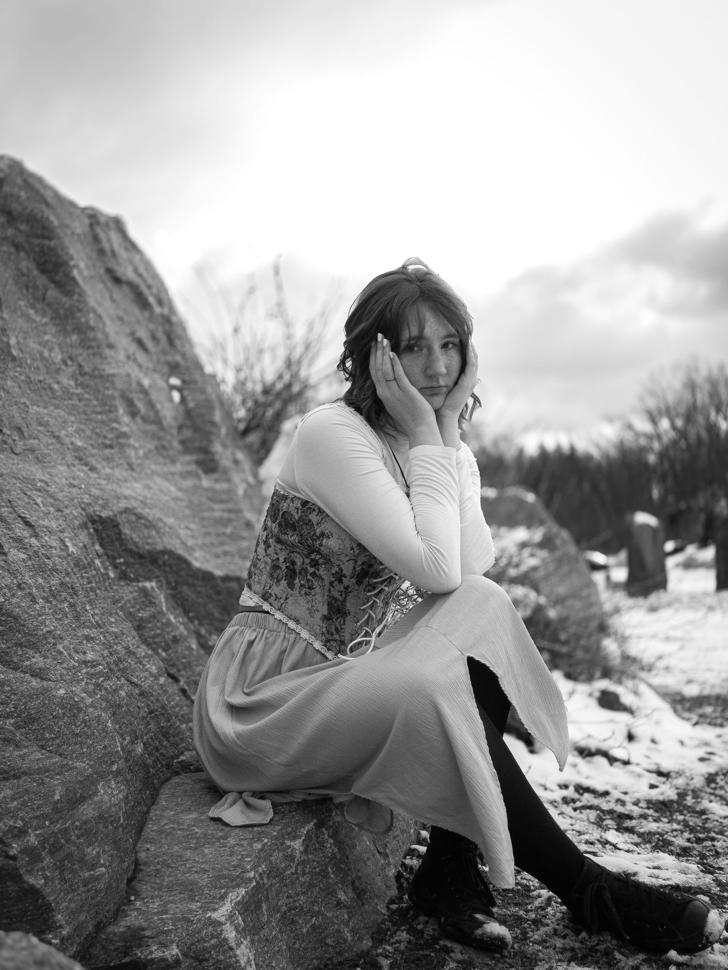 A series of black and white photos showing someone in white clothing sitting thoughtfully on rocky terrain.