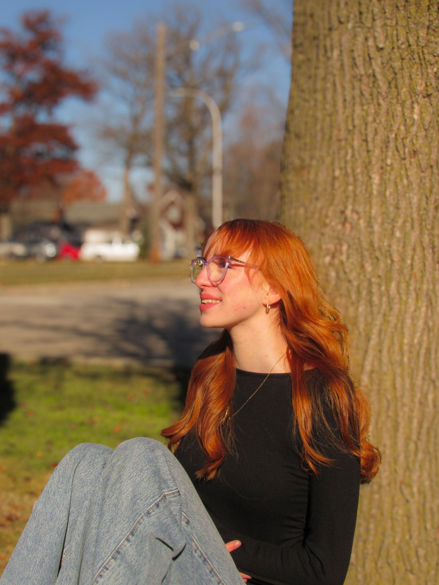 Person with red hair relaxing against a tree trunk in autumn sunlight.