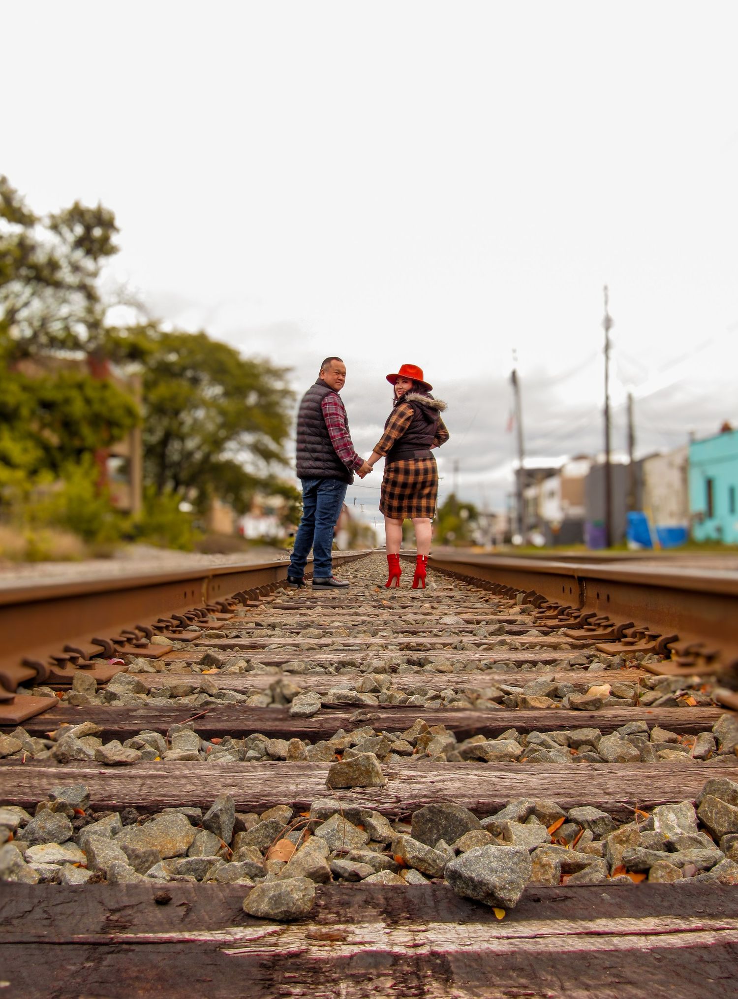 Two people stand together on railroad tracks with a downtown in the background.