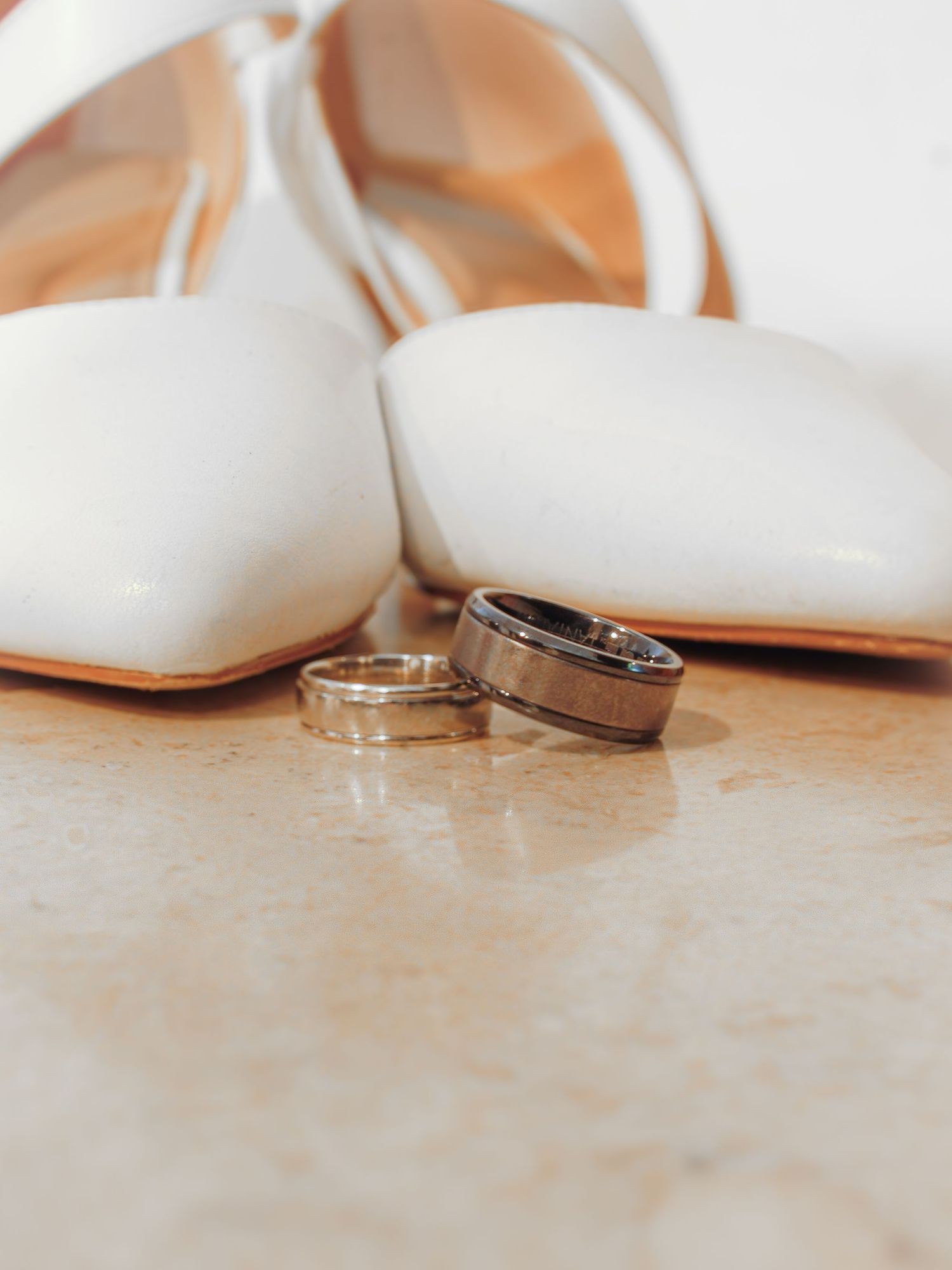 Wedding rings rest on a soft white surface with gentle shadows and romantic lighting.