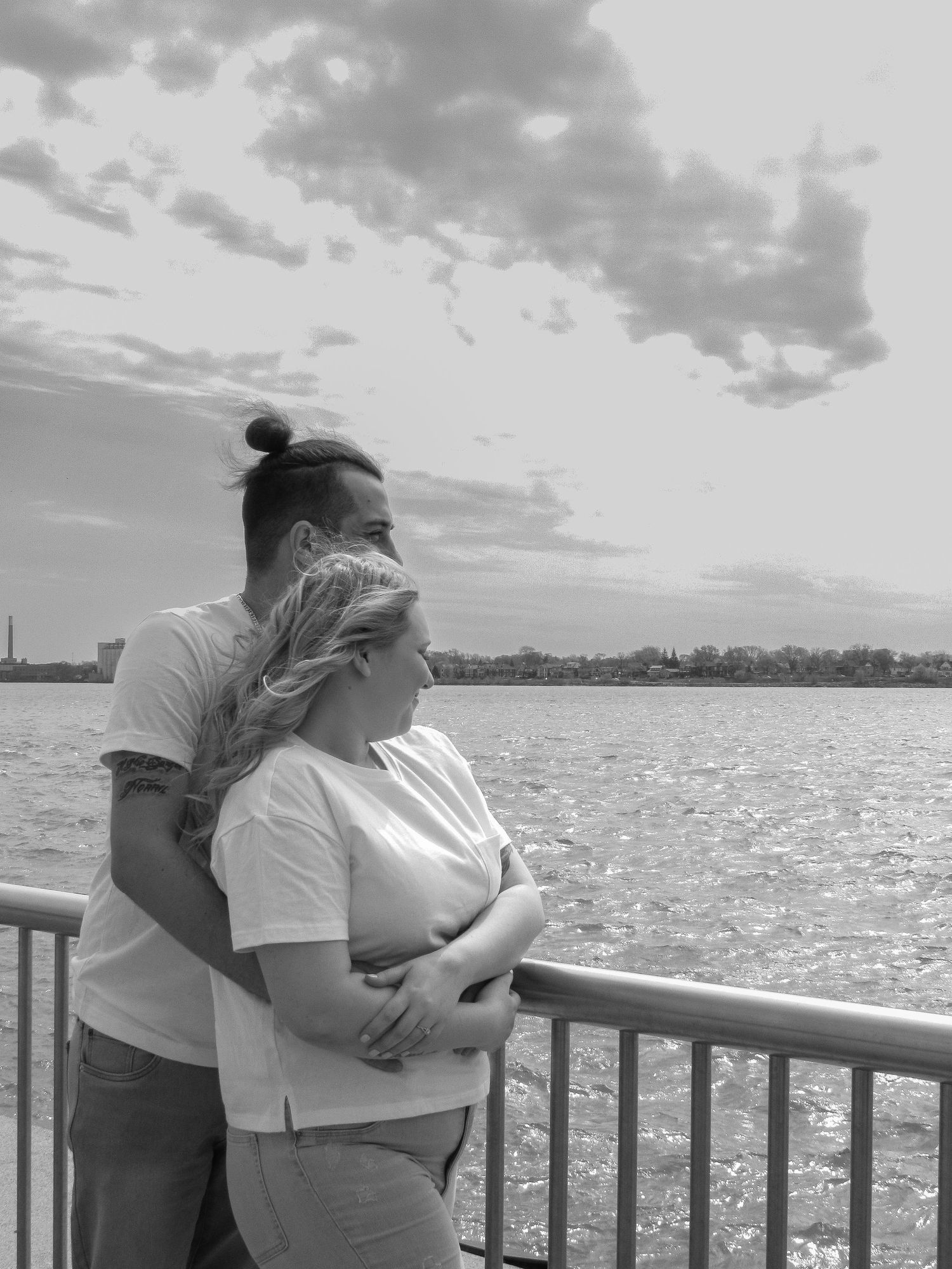 A couple shares a romantic moment on a waterfront deck with sparkling water in the background.