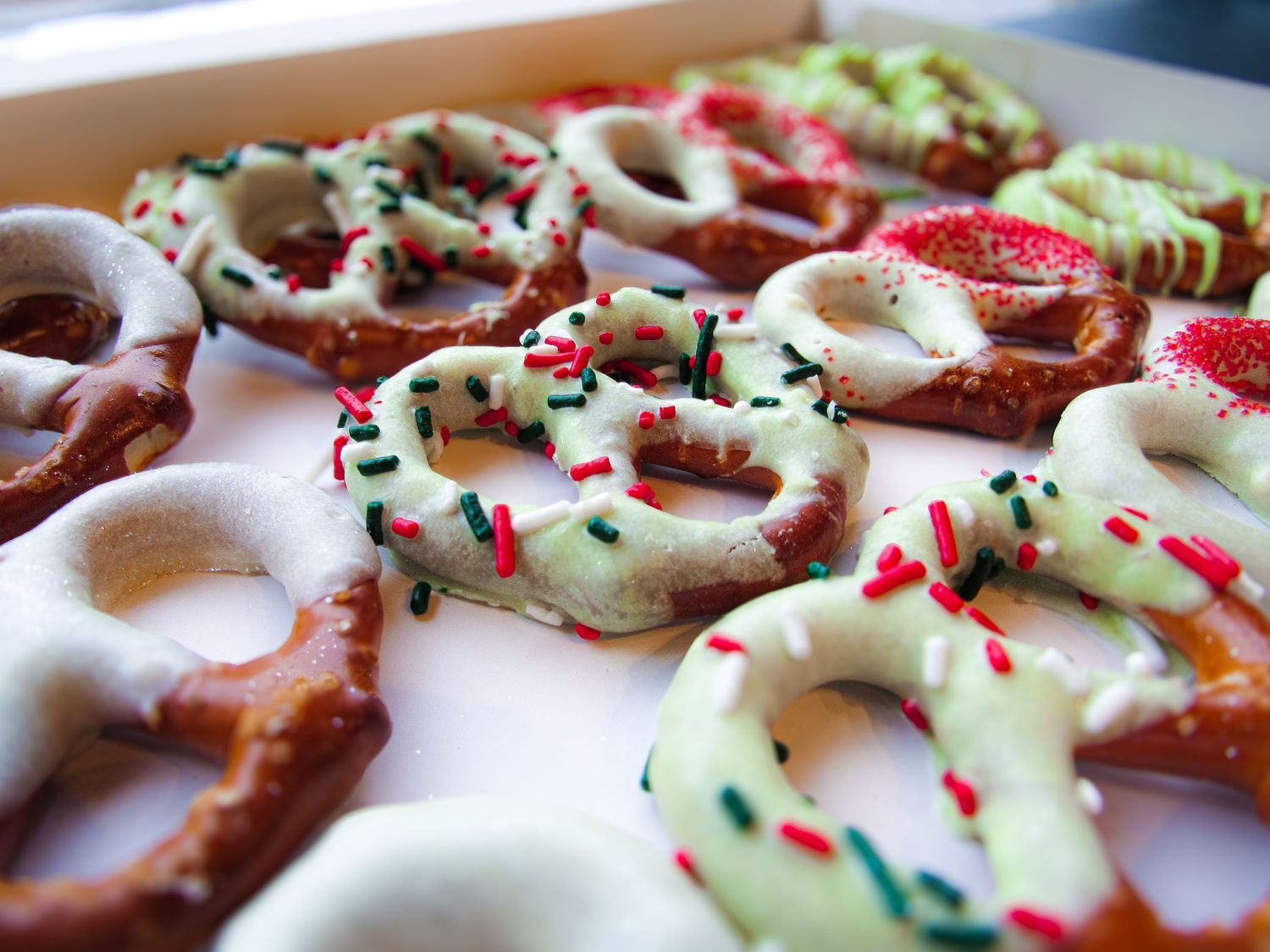 Chocolate and vanilla dipped pretzels decorated with colorful sprinkles arranged on a white surface.