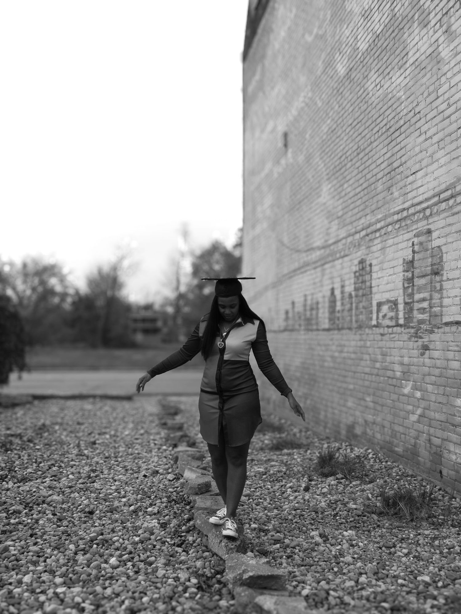 Person walking along a brick wall on rocky ground in black and white photography.