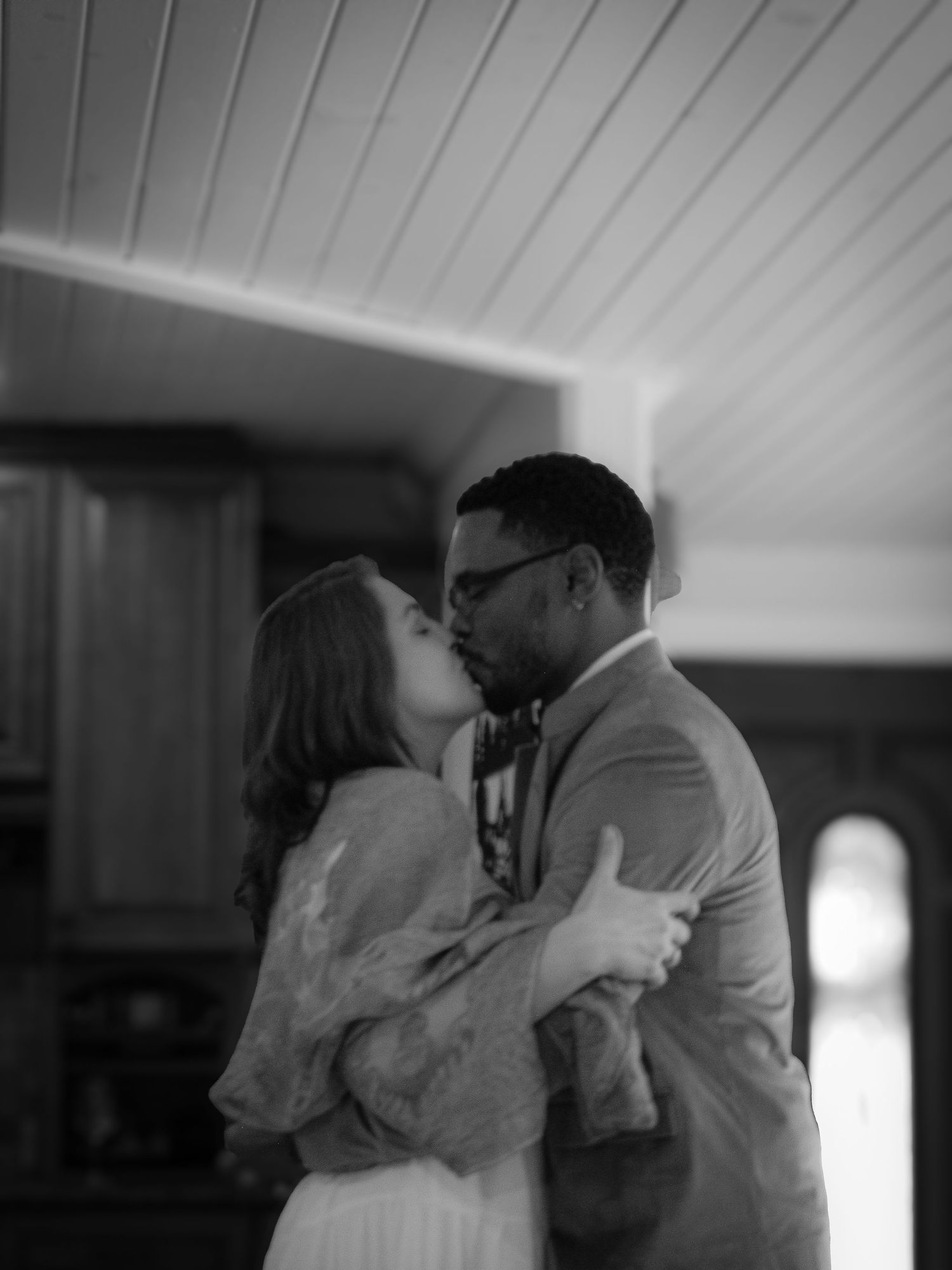 Black and white sequence of a romantic kiss in a sunlit room with white walls.