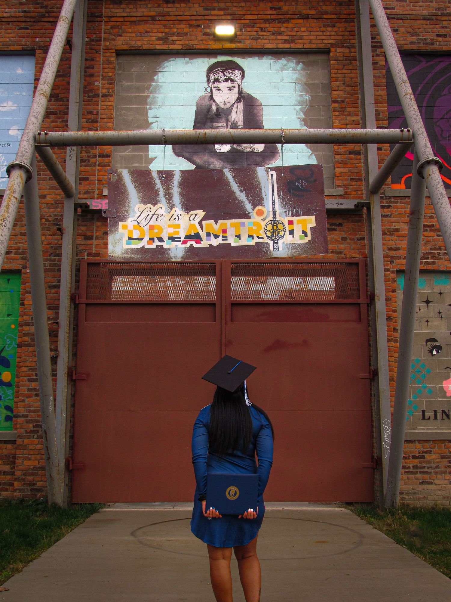 Person in blue sweatshirt and shorts standing in front of brick wall and metal doors at different distances.