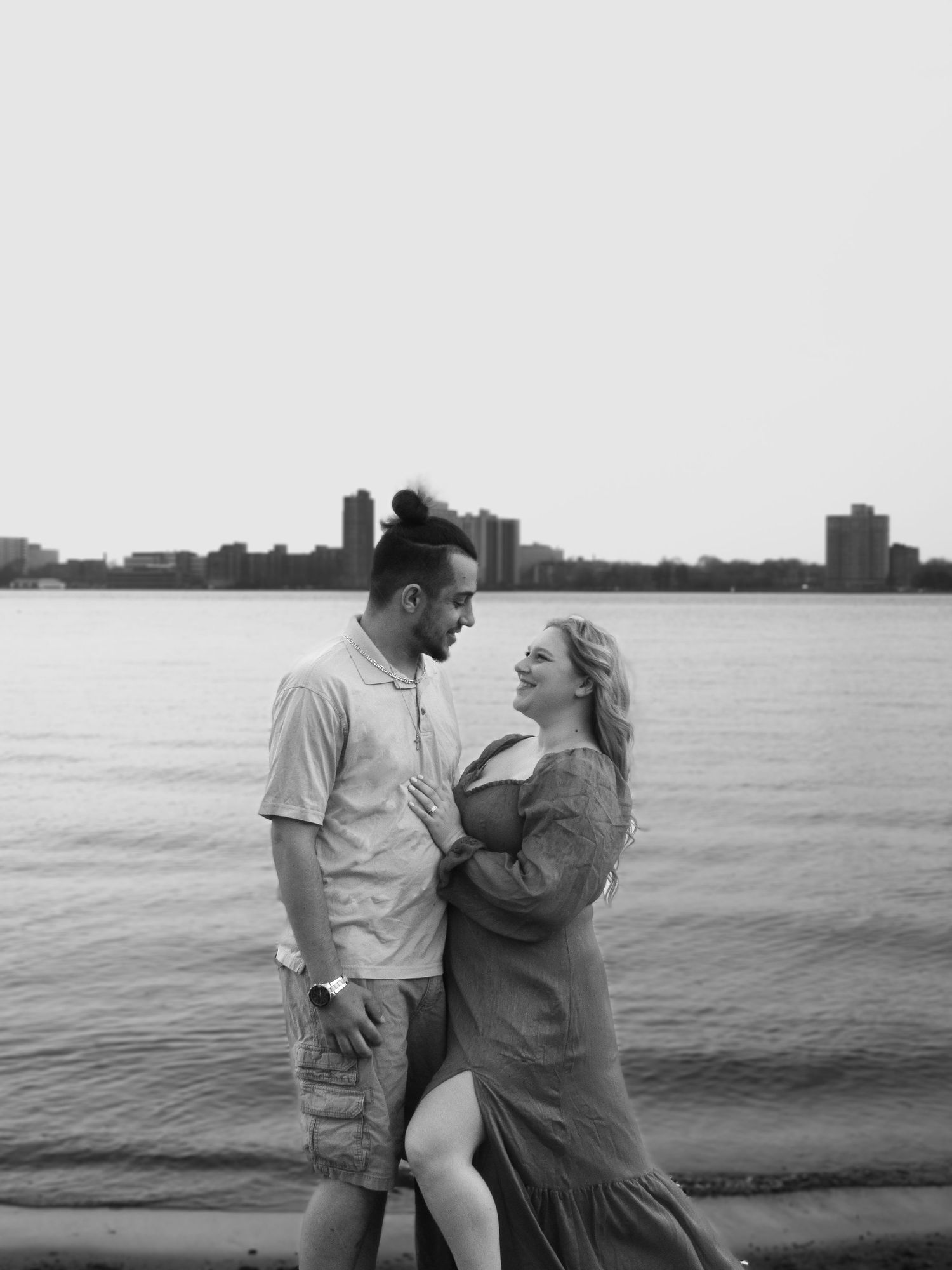 A couple shares a tender moment together by the waterfront during a black and white photoshoot.