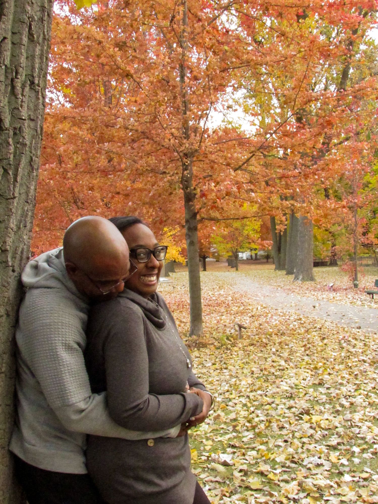 Loving couple embracing in a park surrounded by trees with bright orange fall foliage.