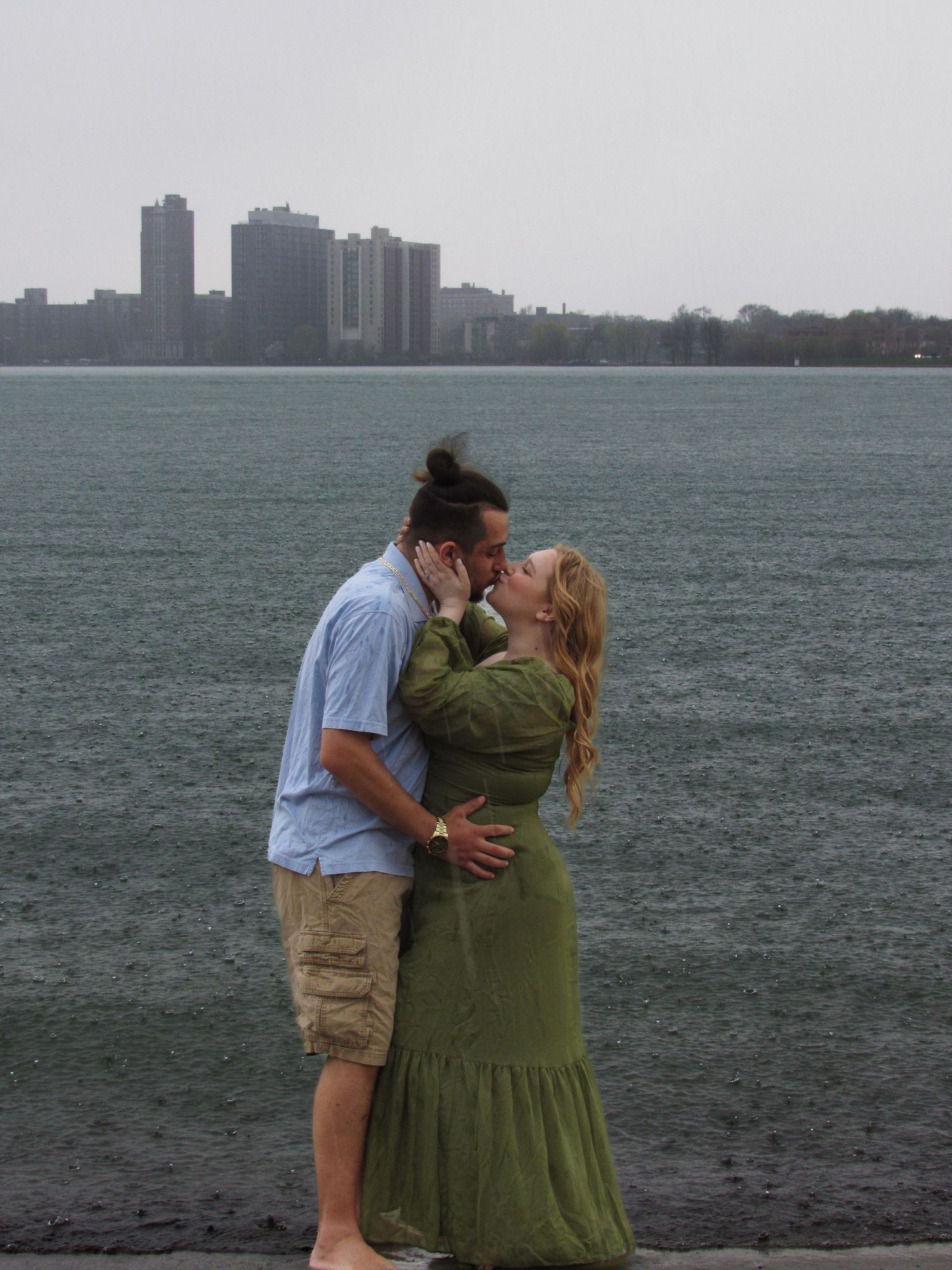 A romantic moment shared by a couple against a cityscape backdrop along the waterfront.