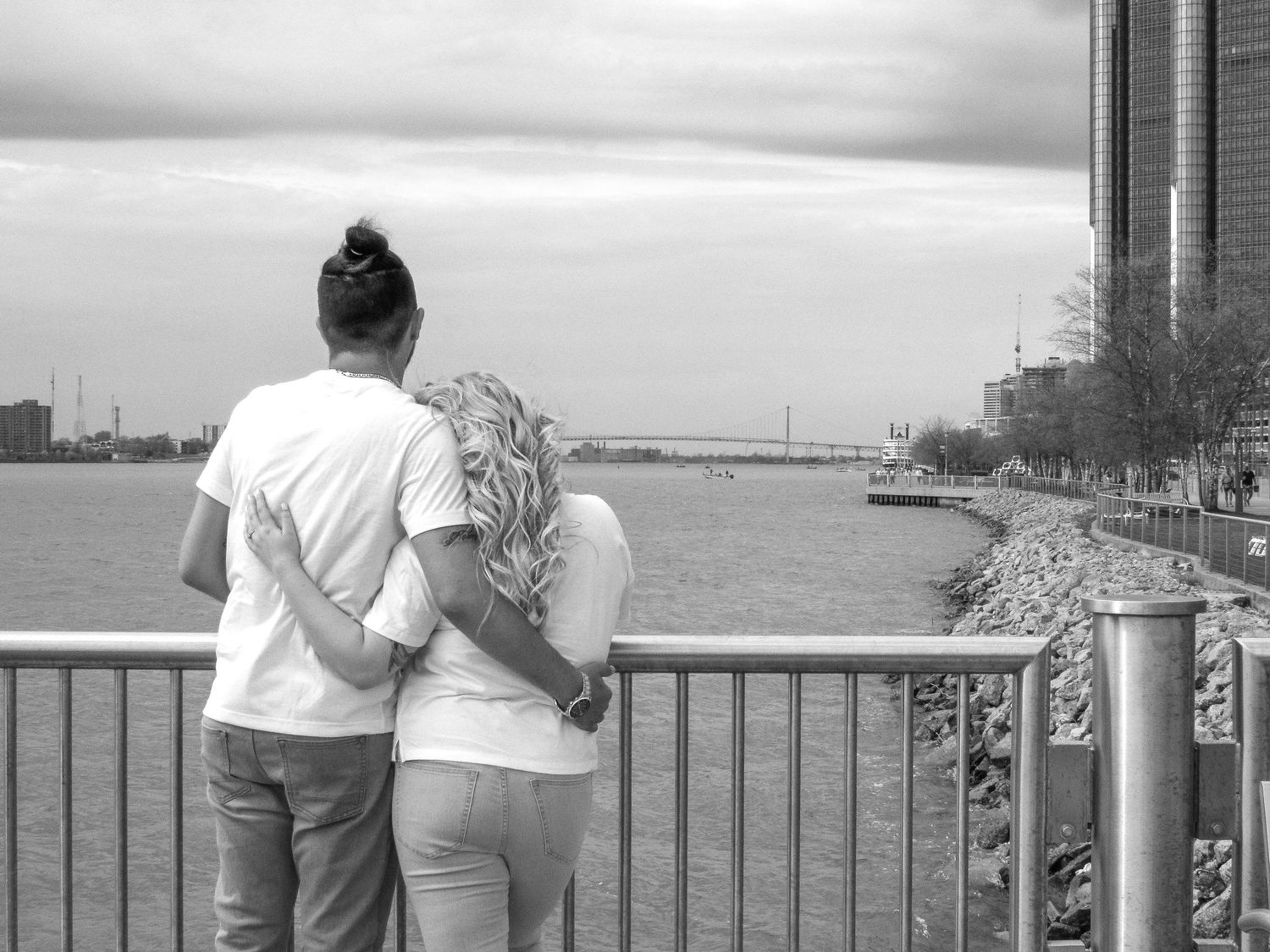 Two people lean against a railing overlooking a scenic waterfront view.