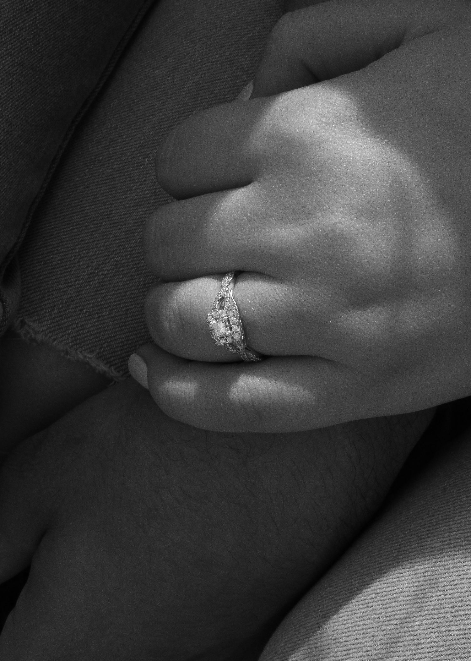 Close-up black and white photo of a diamond engagement ring on a person's finger against a textured background.