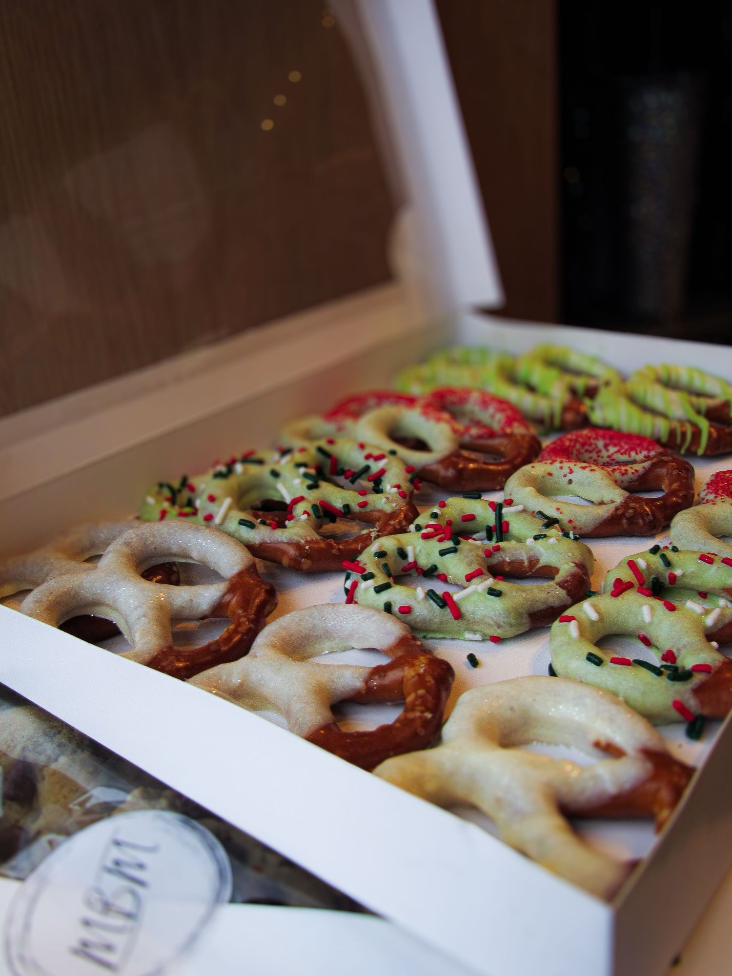 Colorful frosted pretzels with sprinkles and toppings arranged in neat rows inside a white bakery box.