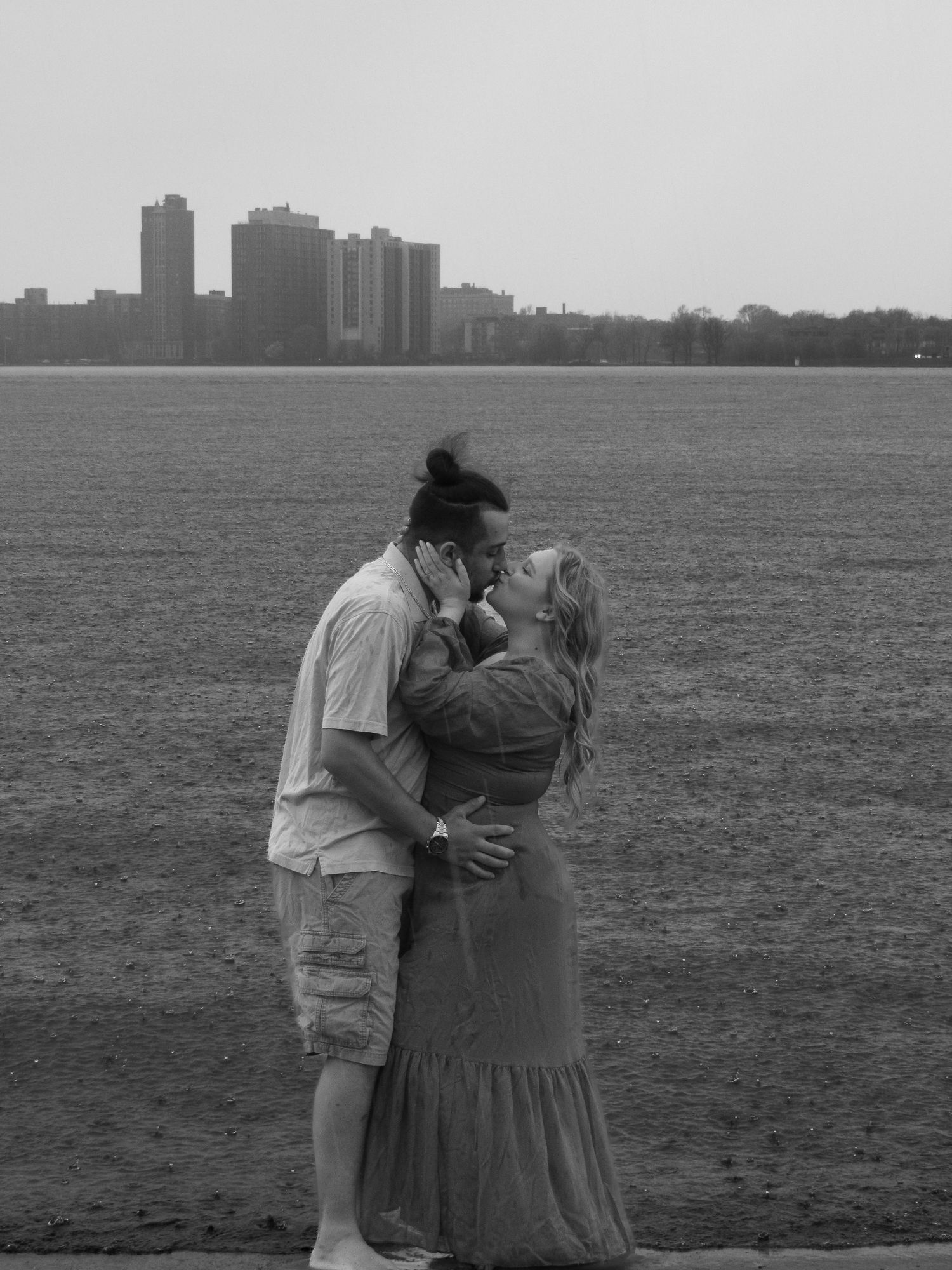 A romantic couple shares a tender moment on a beach with city skyline silhouettes in the background.