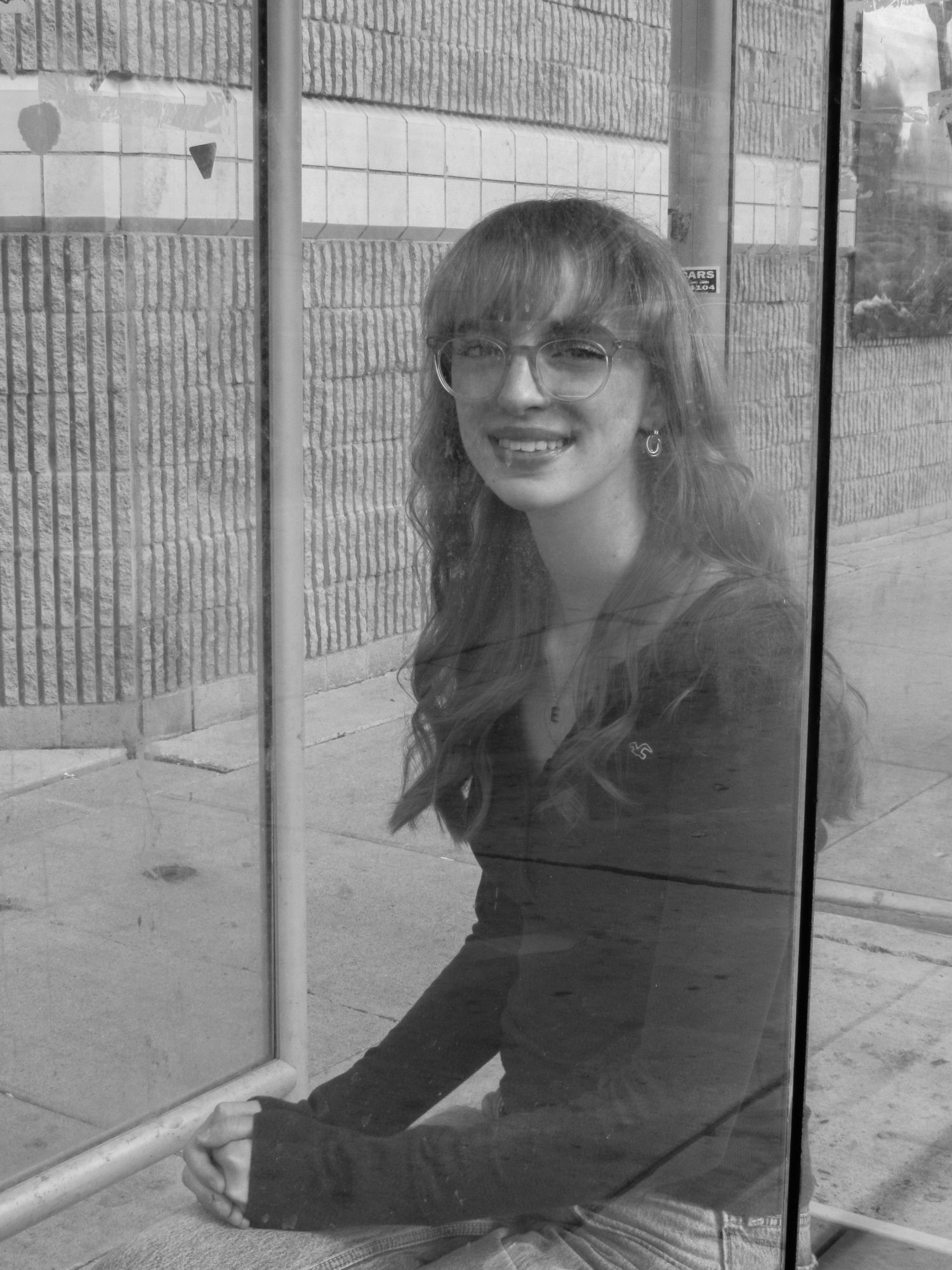Person sitting by a textured wall in black and white photography.