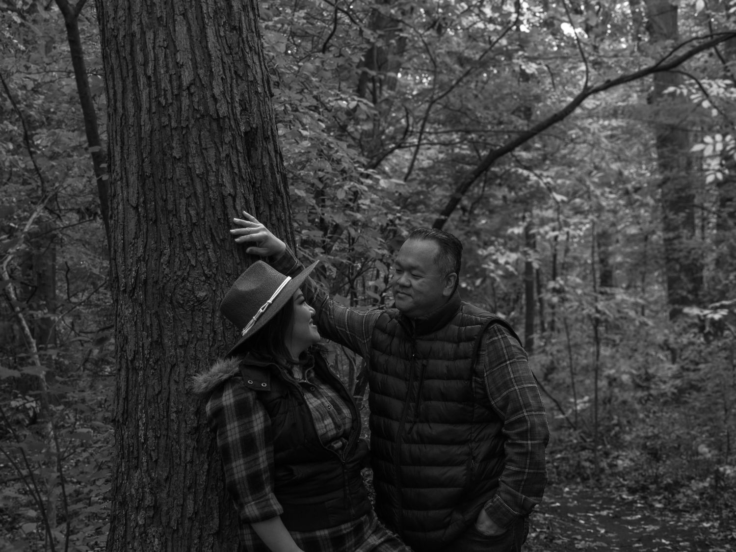 A couple shares a tender moment among trees in a dark forest setting.