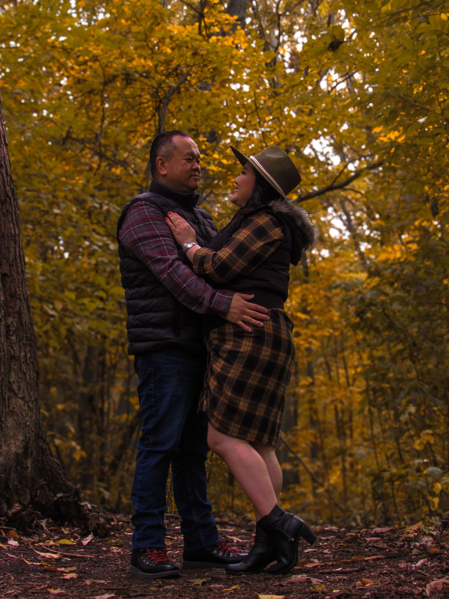 Two people embrace among autumn trees with golden leaves in a forest setting.