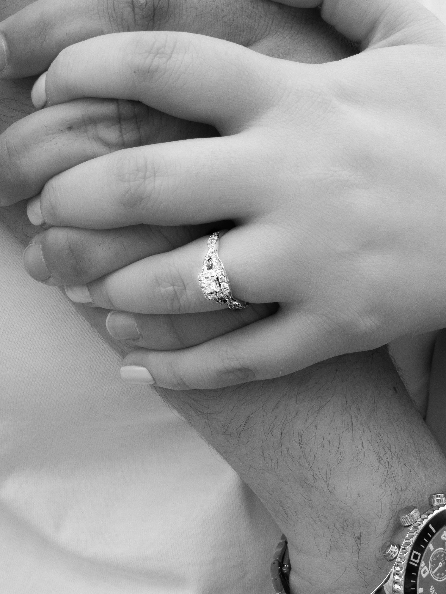 Close-up black and white photo of hands with an engagement ring featuring a sparkling diamond setting.