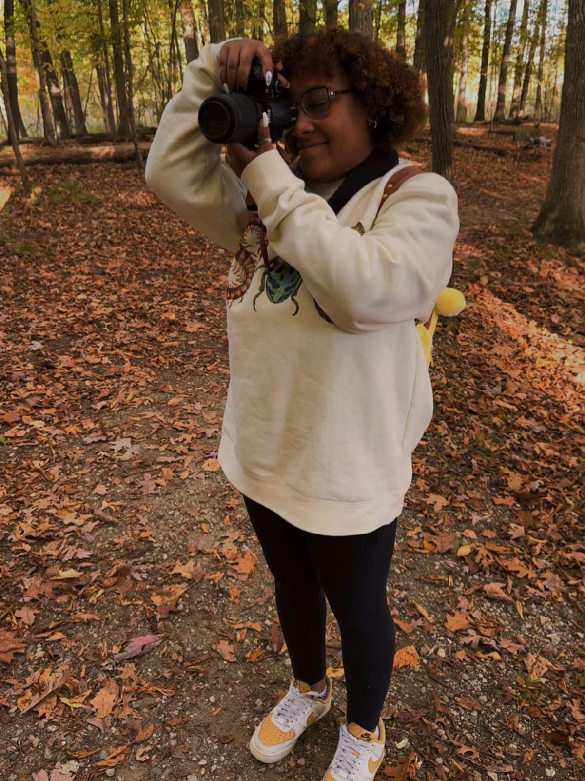 A photographer captures autumn scenes in a wooded area with fallen leaves.