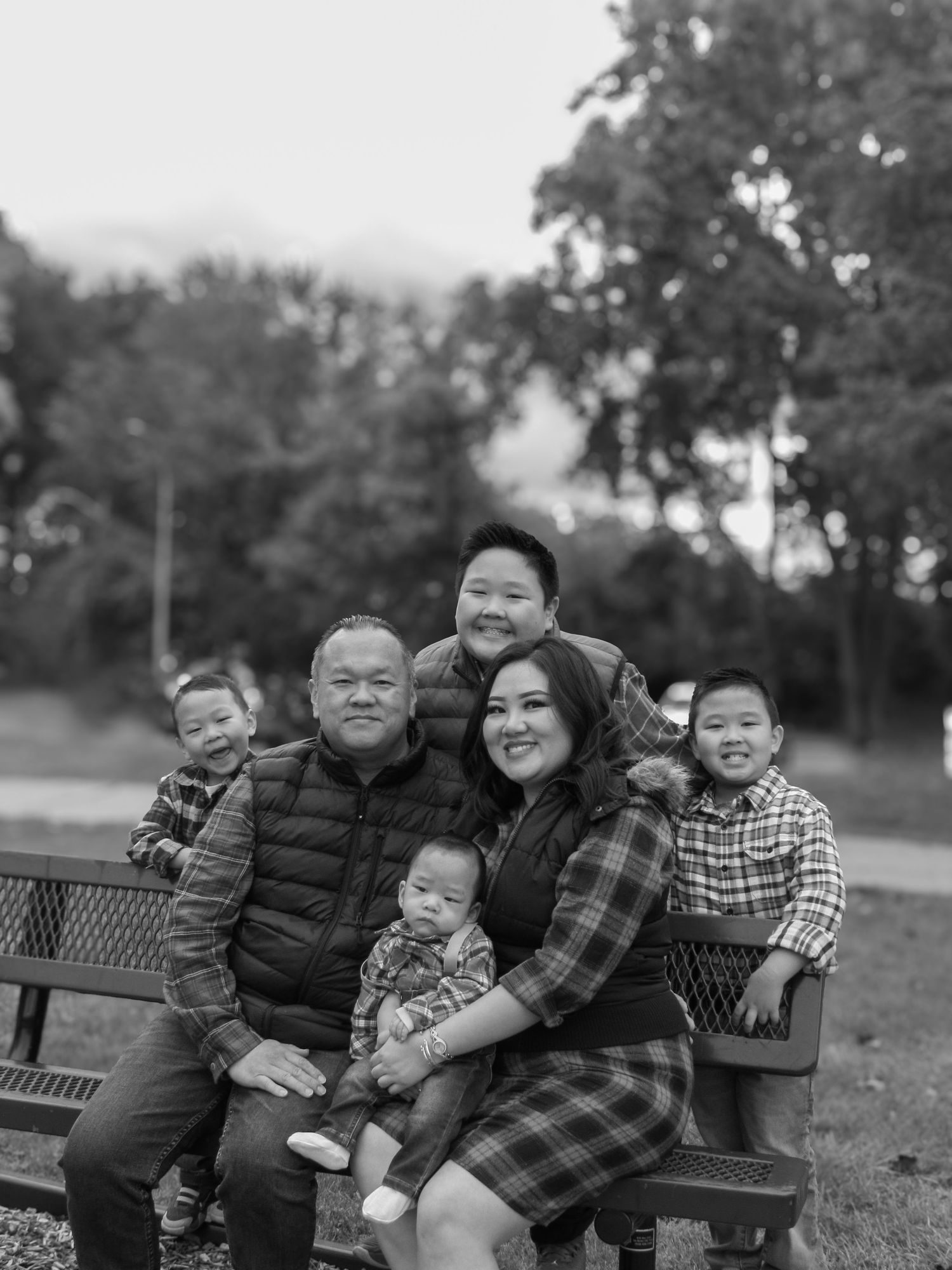 A heartwarming family portrait of six people sitting together on a park bench in black and white.