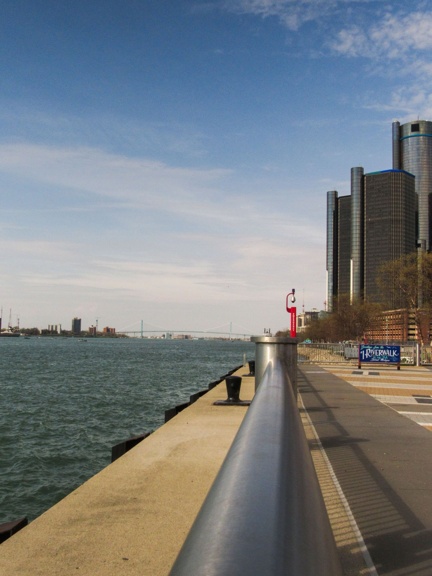 Detroit's Renaissance Center towers along the riverfront with a metal railing in the foreground.