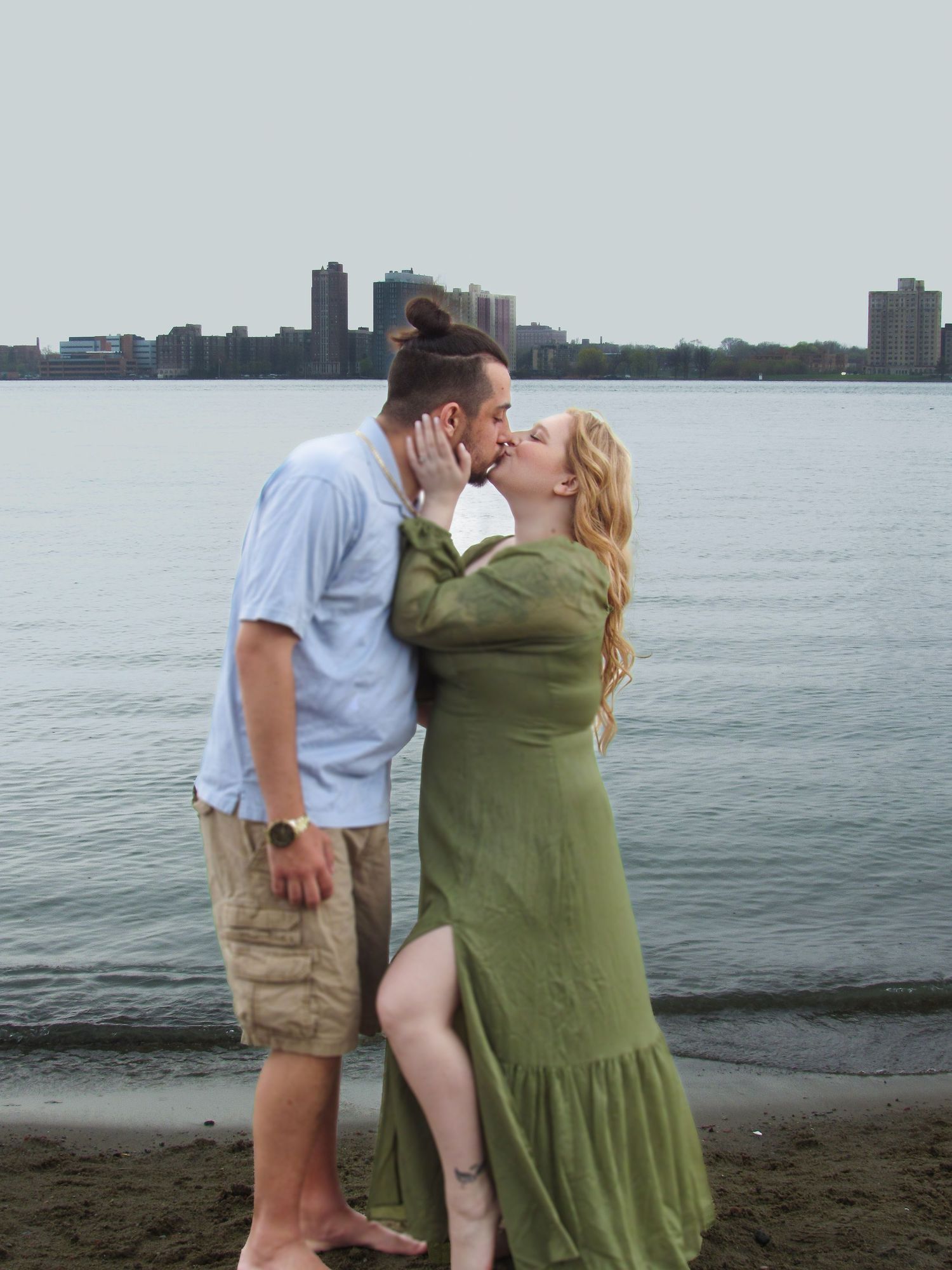 Romantic couple embracing at sunset by the waterfront with city skyline in the background.