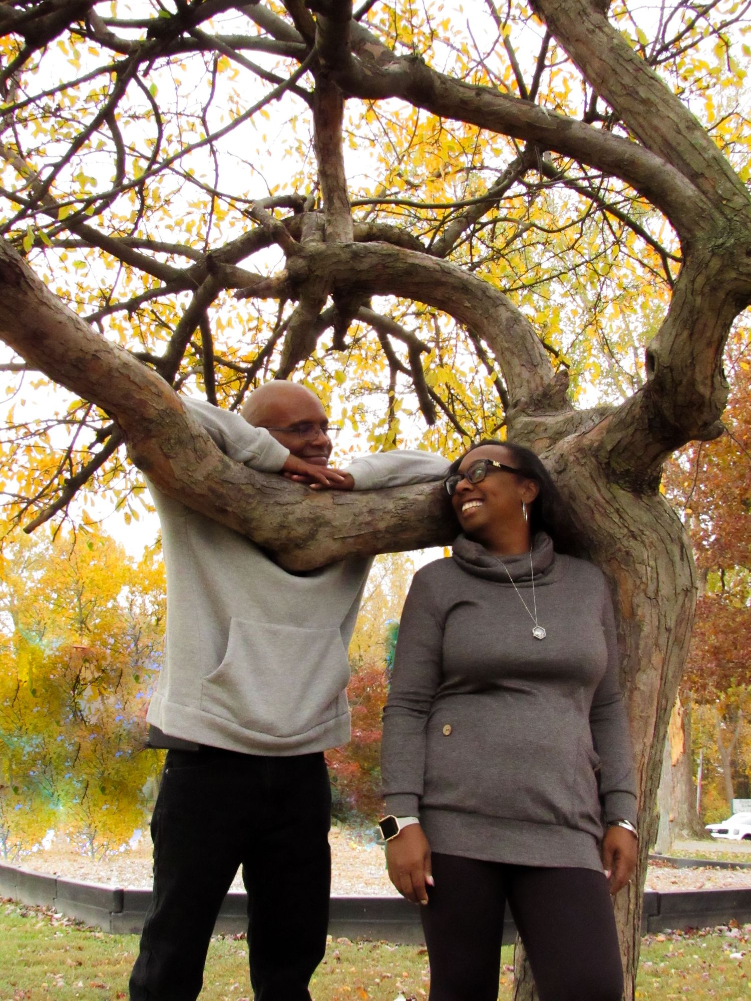Playful couple posing against autumn trees with golden leaves in the background.